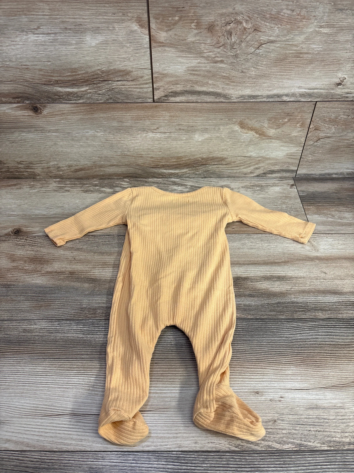 Beige ribbed long sleeve footed baby sleeper laid flat on wood floor