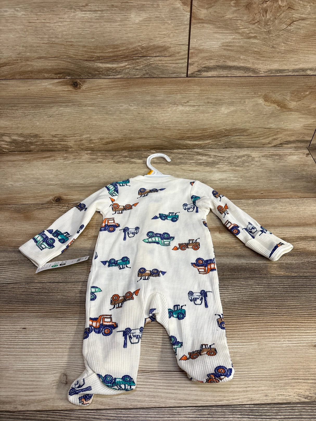 White baby romper with colorful trucks and cars print, laid flat on wooden floor