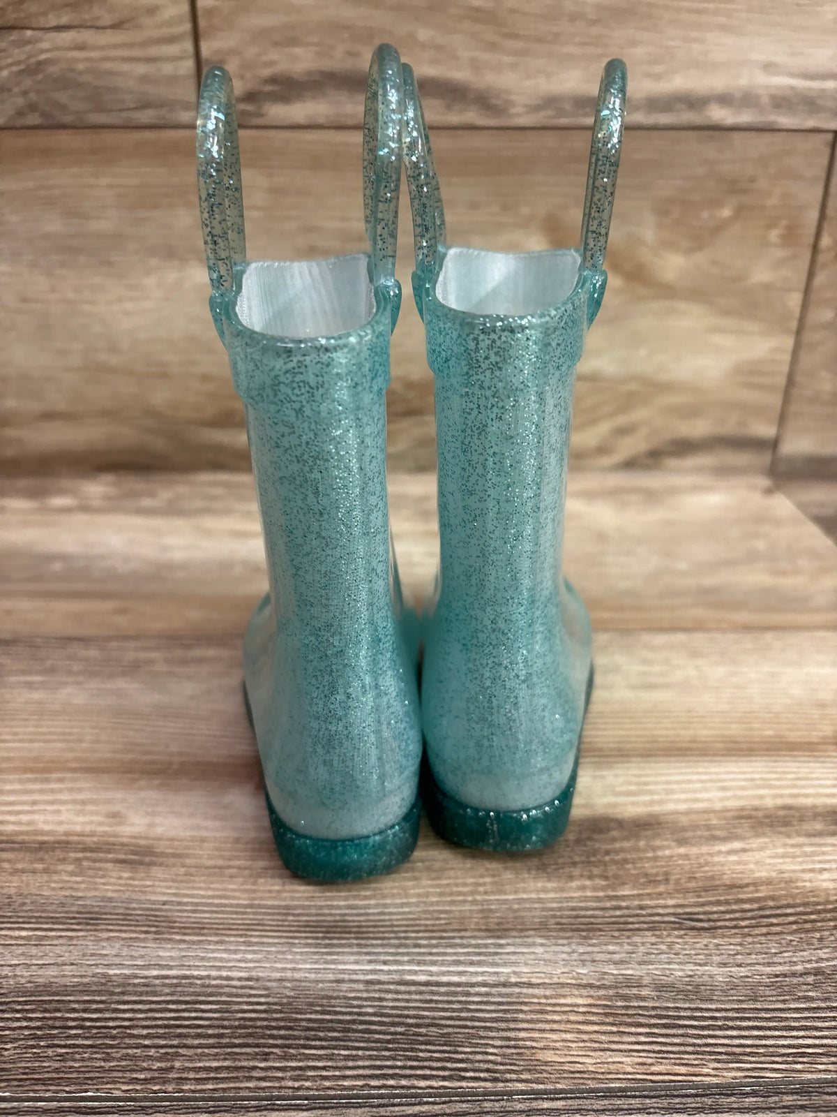 Front view of Disney Elsa seafoam glitter Wellington boots with pull-on handles and dark teal soles on a wood floor