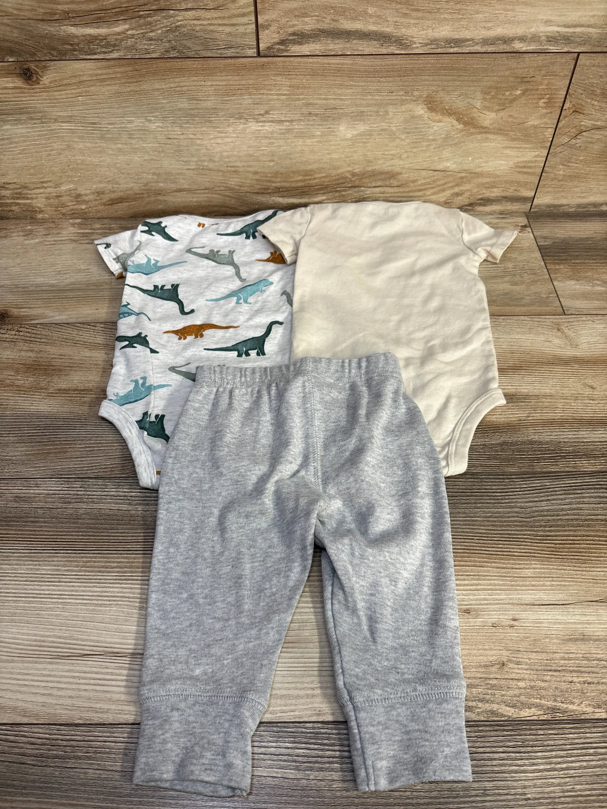 Overhead view of Child Of Mine 3pc bodysuit and pants set, with dinosaur-print and plain bodysuits plus gray pants