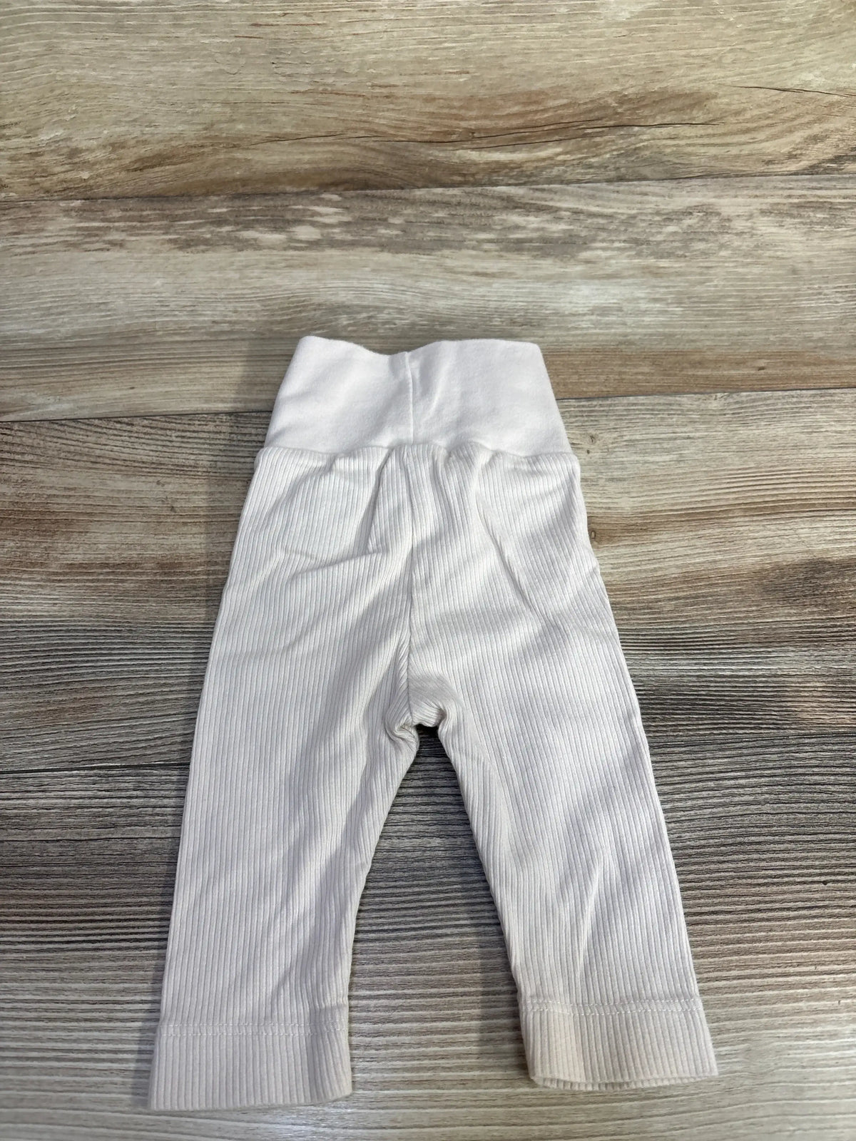 Flat lay of newborn ribbed foldover-waist baby pants showcasing ribbed texture and wide foldover waistband on wood background