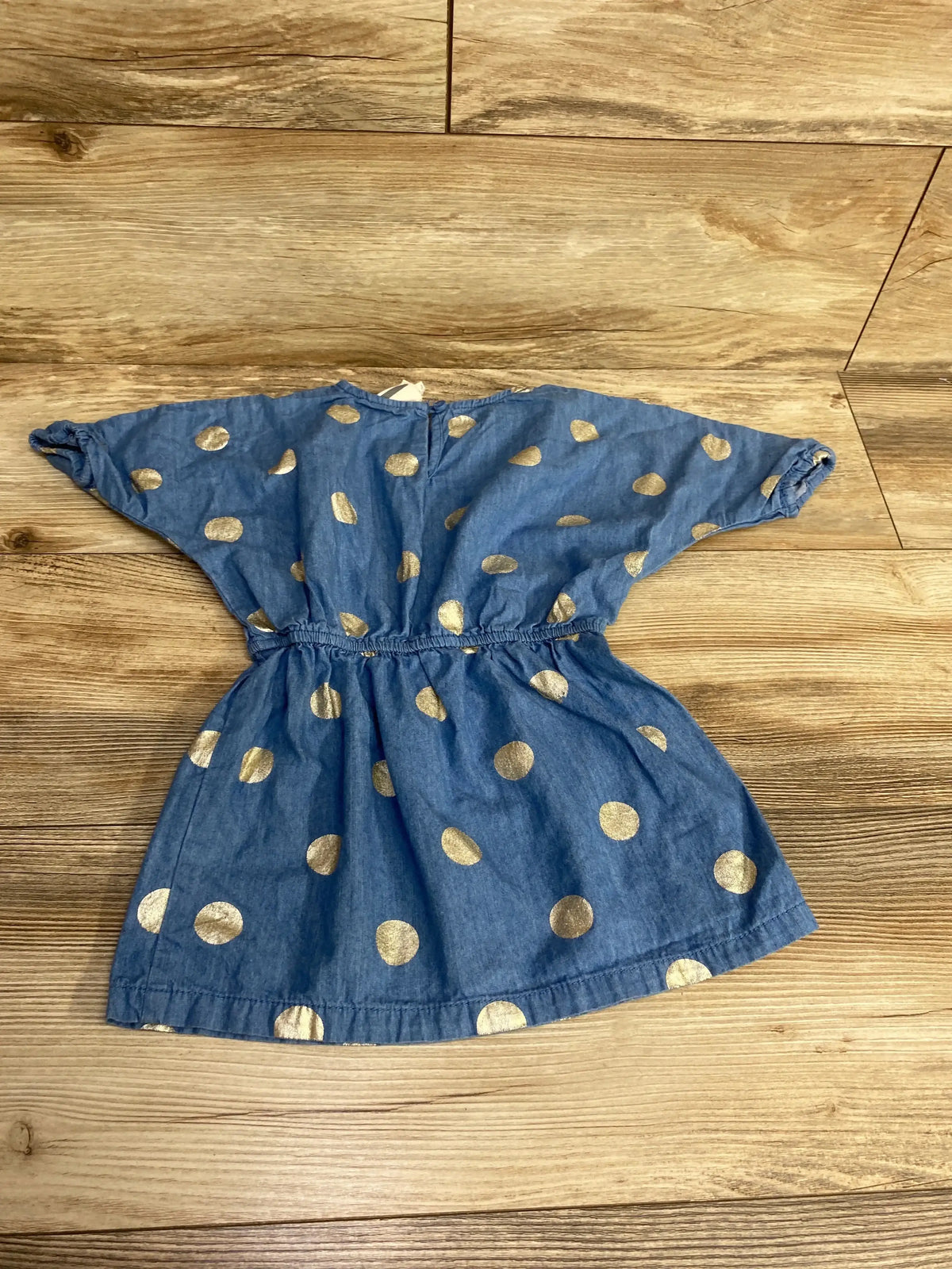 Blue children's dress with gold polka dots, short sleeves, and elastic waist on wooden floor