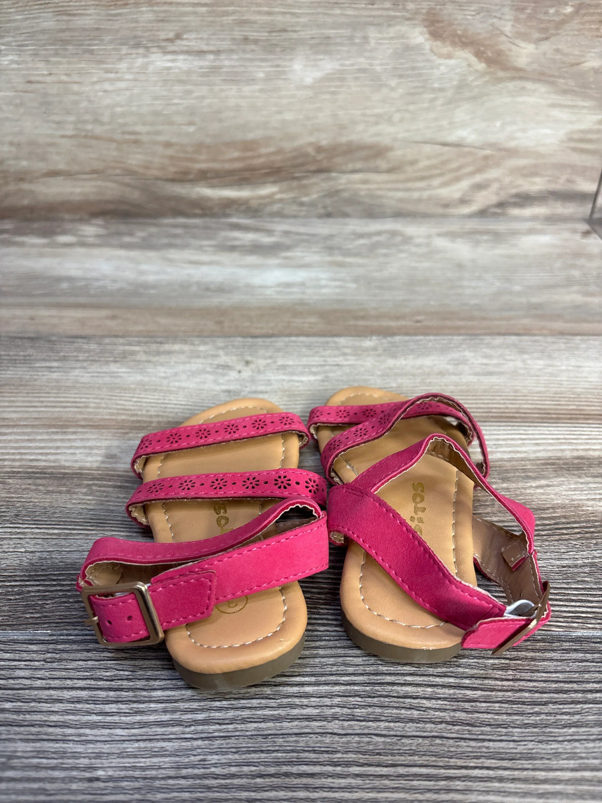 Top view of Ositos pink slingback sandals showing three perforated straps and an adjustable buckle on wood background