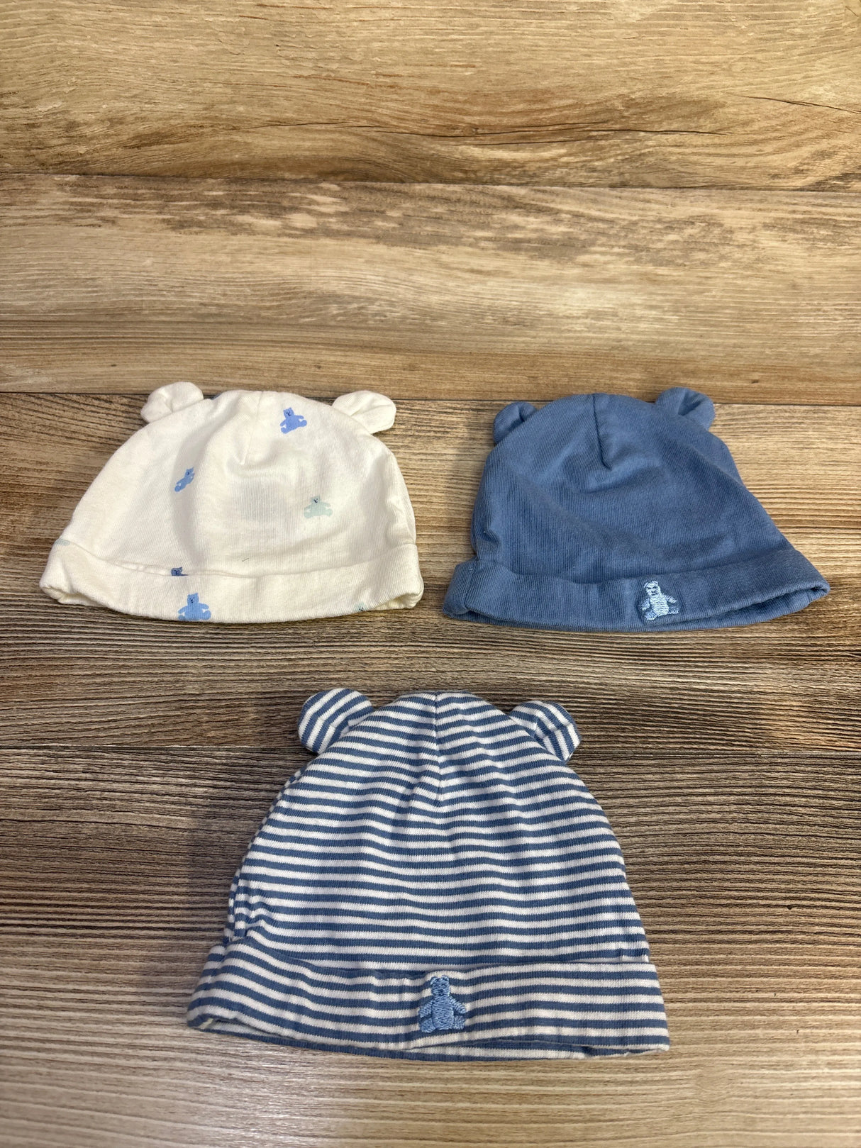 Front view of three Baby Gap organic cotton beanies with bear ears, blue and cream printed and striped designs