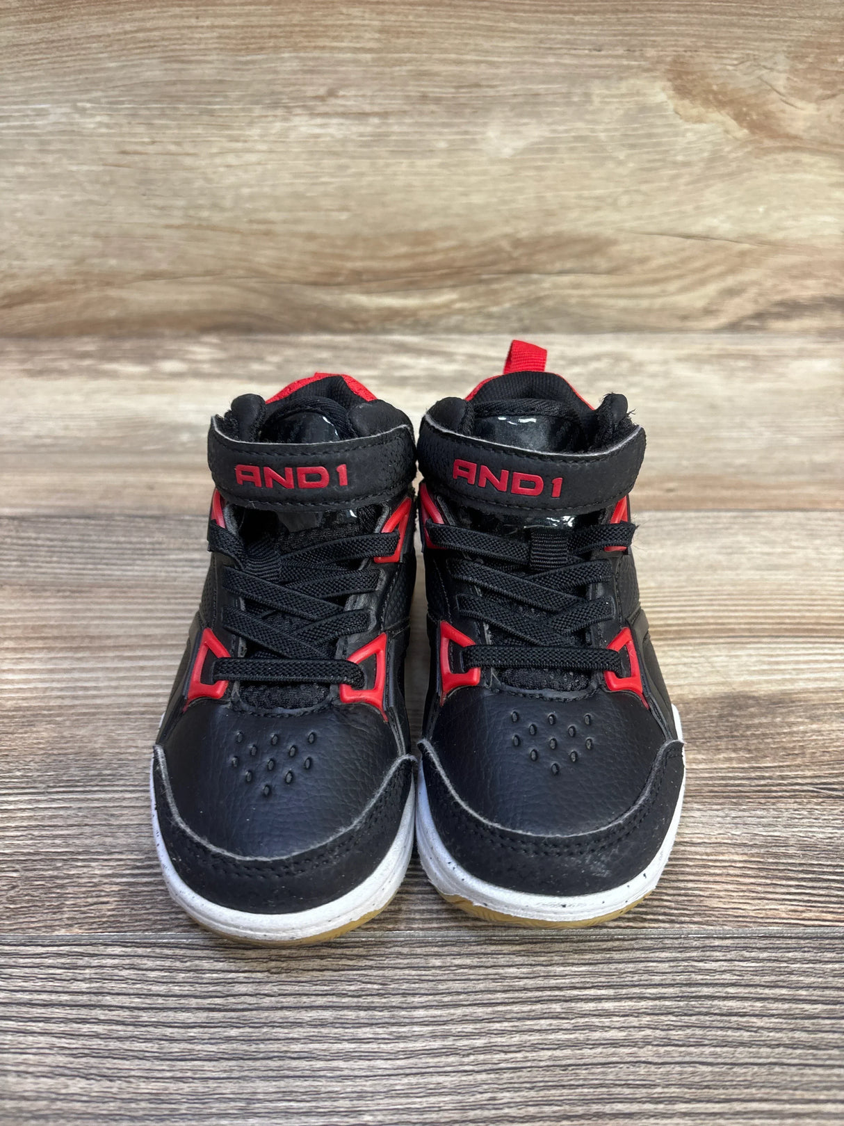 Front view of toddler AND1 black lace-up basketball sneakers showing red accents and Velcro ankle strap on wood background