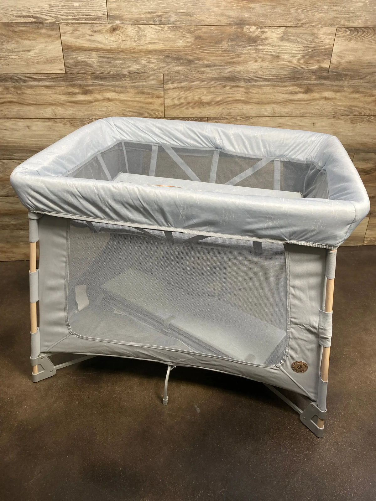 Three-quarter view of Maxi-Cosi Swift Playard in classic slate with mesh sides, padded top rail, and wood-tone legs