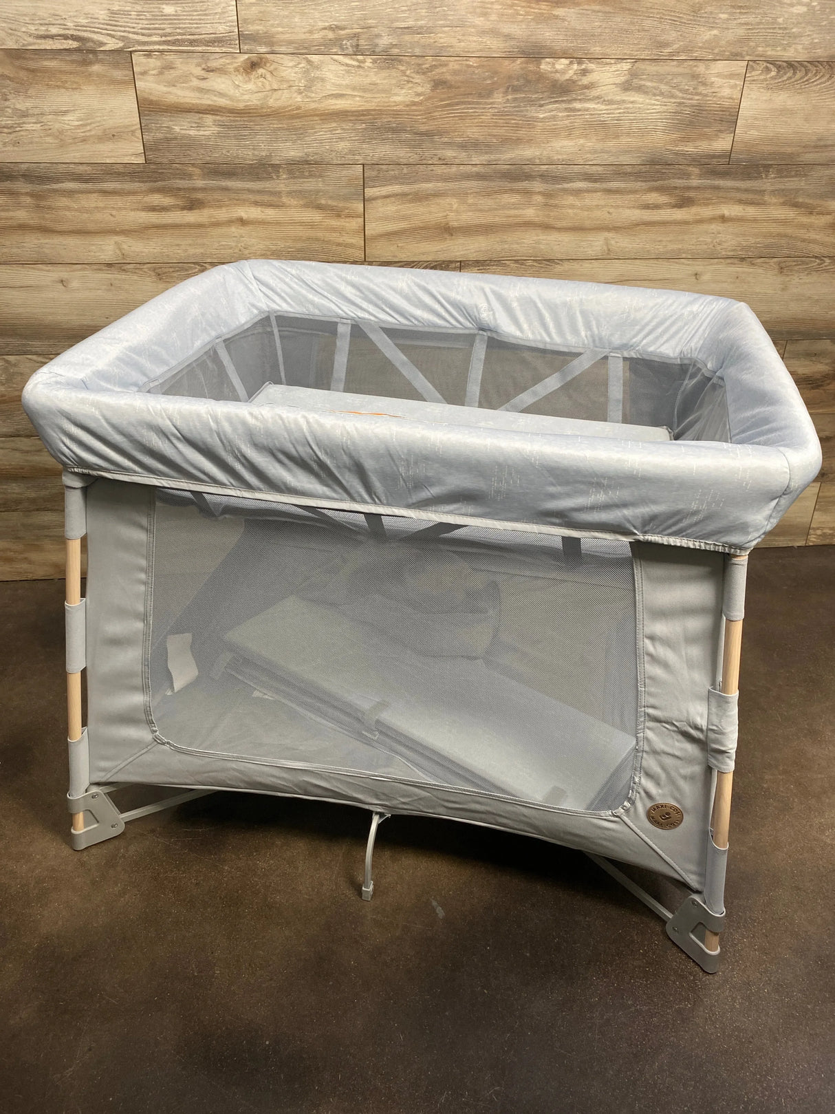 Three-quarter view of Maxi-Cosi Swift Playard in classic slate with mesh sides, padded top rail, and wood-tone legs