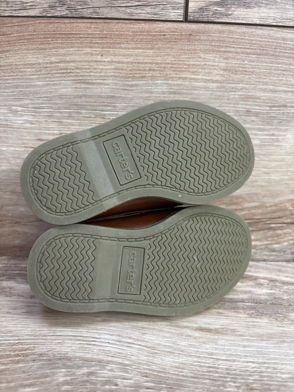 Pair of children's Carter's shoes showing the clean rubber soles with zigzag tread pattern on wooden floor