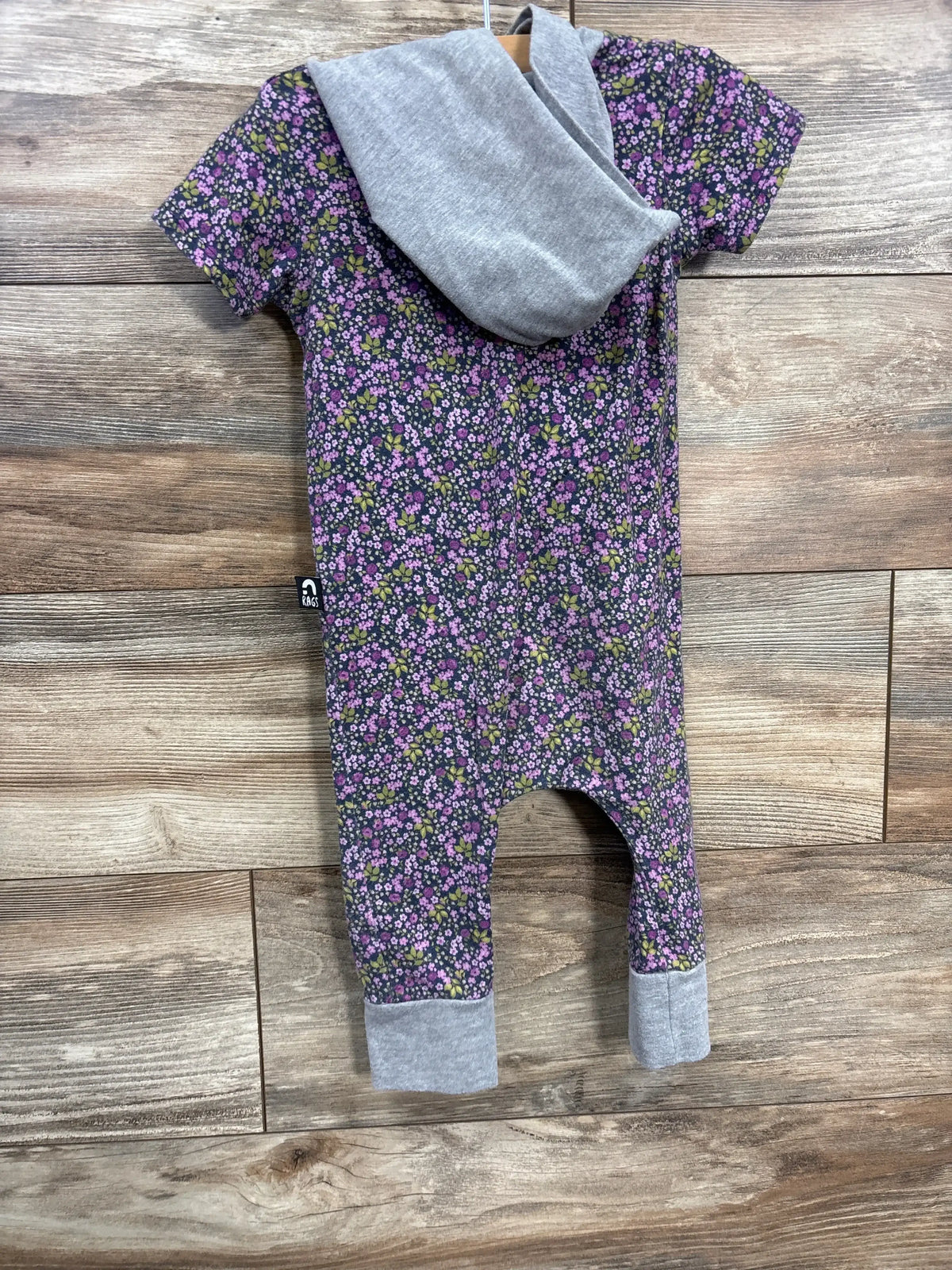 Back view of purple floral hooded romper size 18-24 months showing grey hood and fold over cuffs on wood background