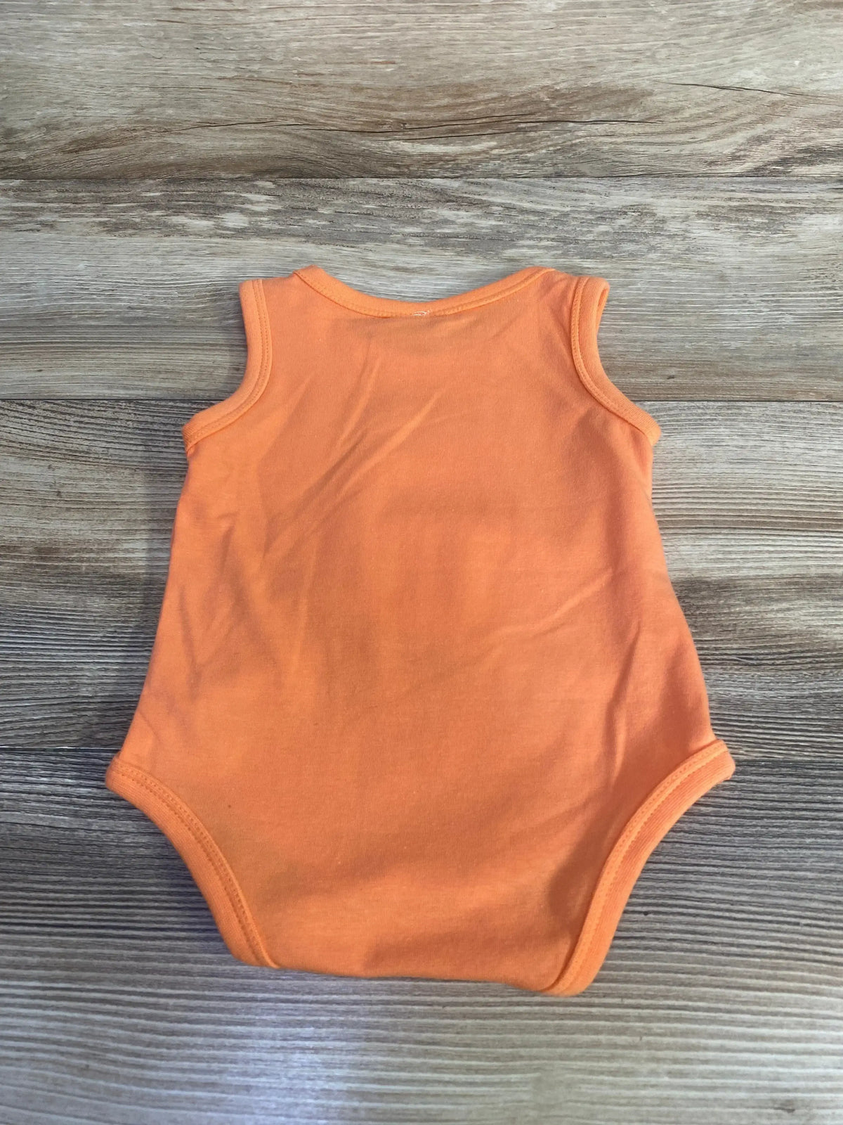 Back flat lay of orange tank-style baby bodysuit in 6-month size showing sleeveless ribbed trim and leg openings on light wood background