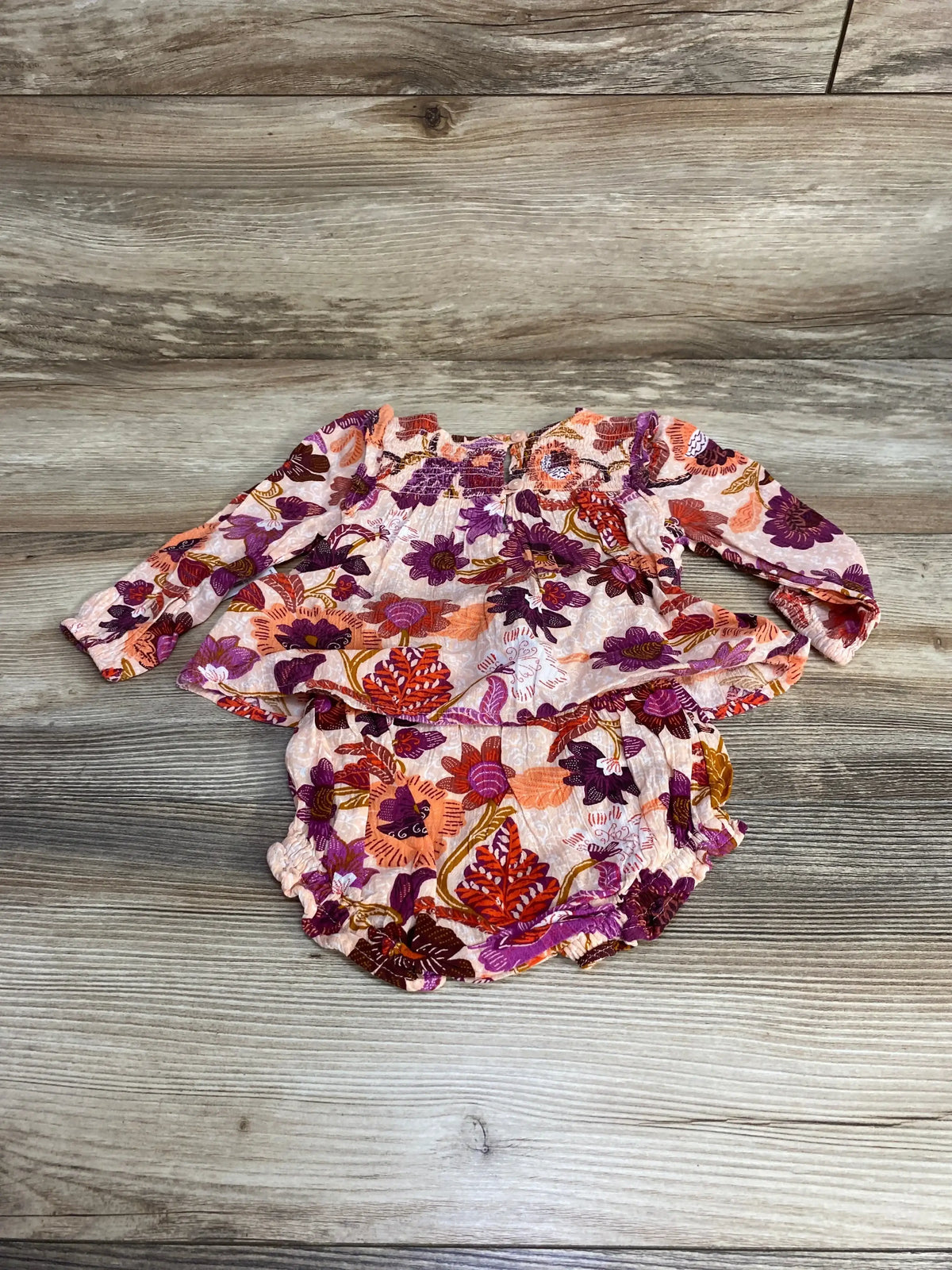 Flat lay of pink Old Navy 2-piece baby set with floral long-sleeve top showing smocked chest and matching bloomers on wood plank background
