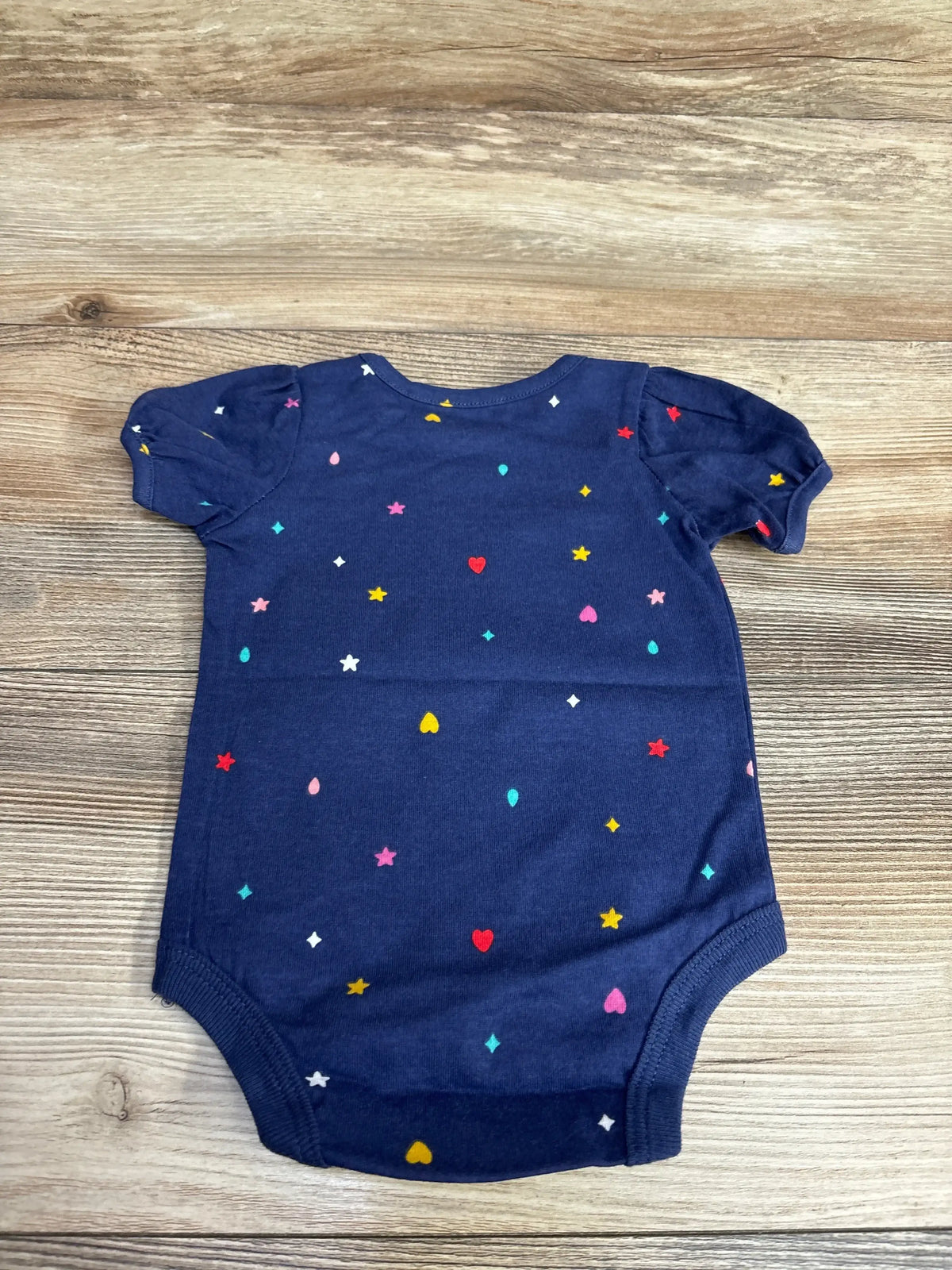 Navy blue baby onesie with colorful heart, star, and teardrop patterns on wooden floor