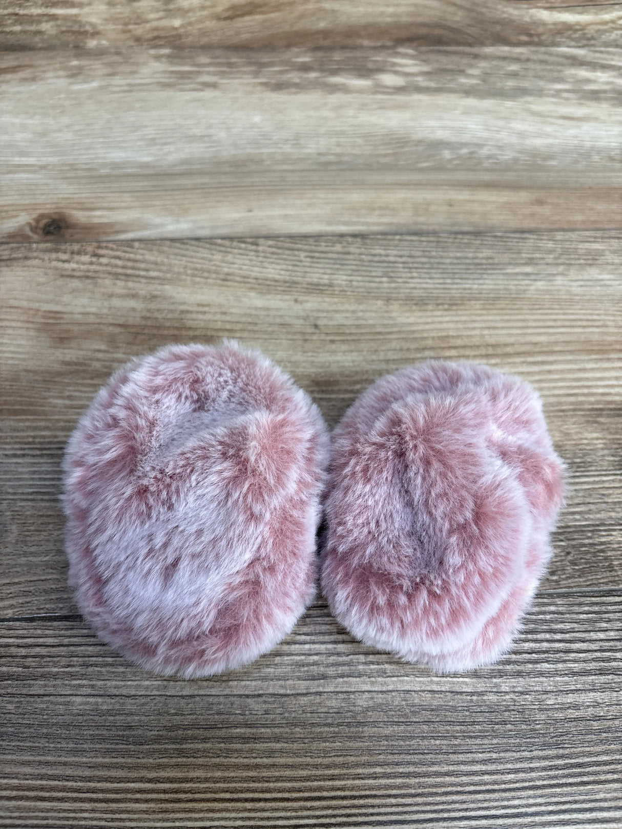 Pair of soft pink faux fur slippers on wooden floor
