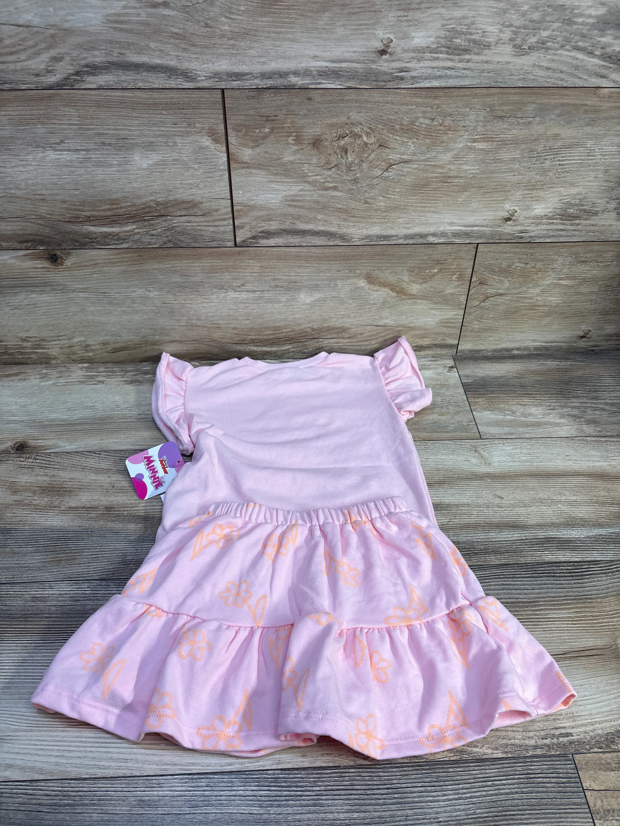 Flat lay of Minnie Mouse pink 2-piece shirt and tiered skort (size 4T) showing ruffle sleeves and orange floral print on wood background