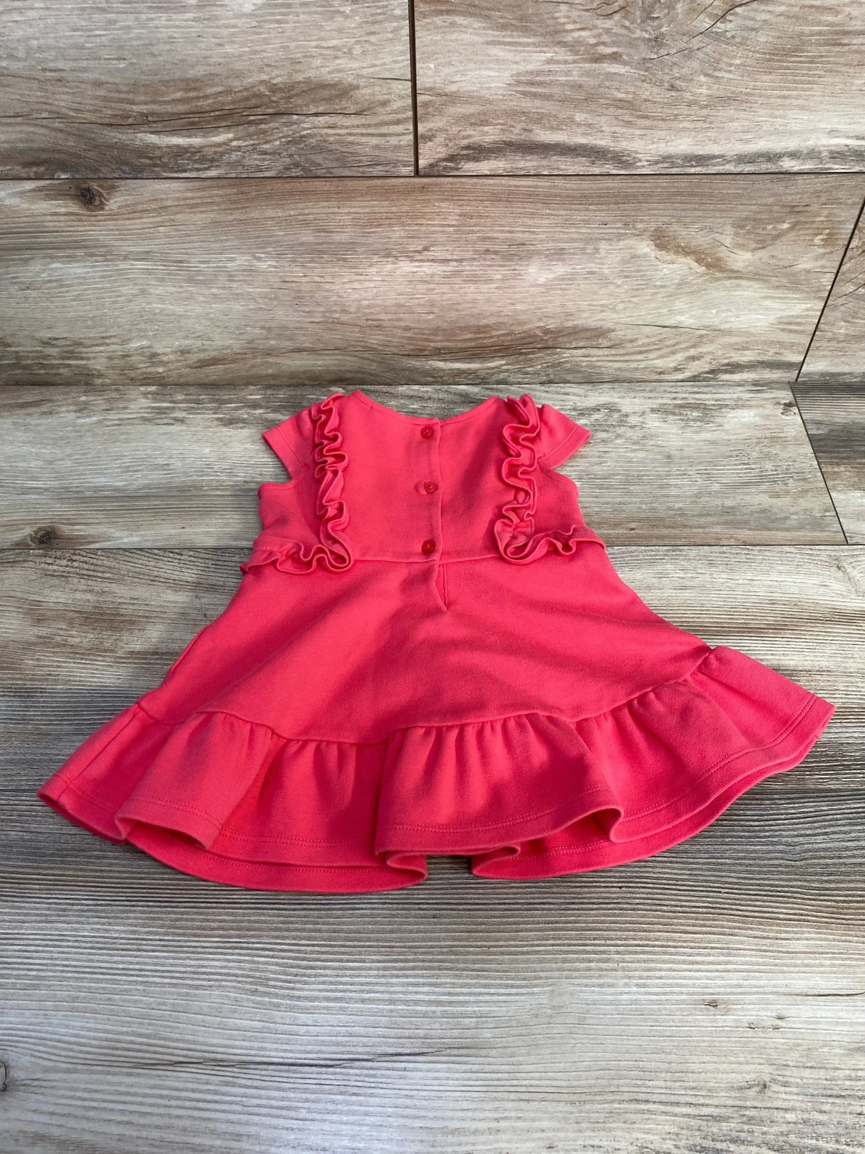 Back view of Janie and Jack ruffle dress size 6 to 12m showcasing coral pink fabric with ruffle trim shoulders and tiered hem on wood plank floor