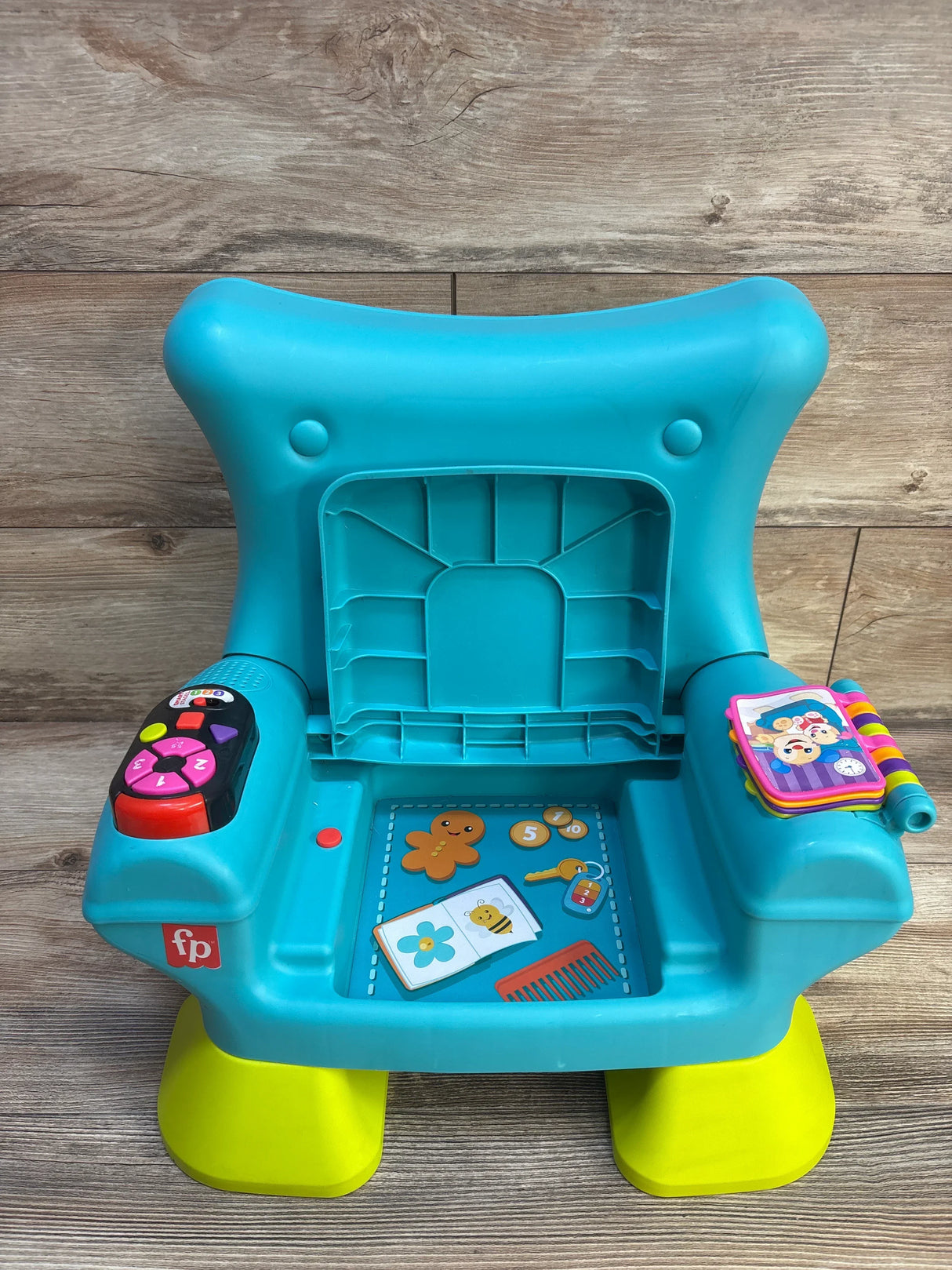 Front view of Fisher-Price Laugh & Learn chair in teal showing interactive buttons on left arm and toy book on right on wood floor