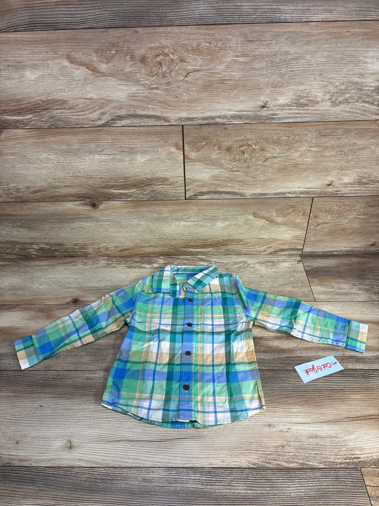 Front of Cat & Jack green plaid button-up shirt size 3T showing long sleeves, chest pocket, and buttons on wooden floor