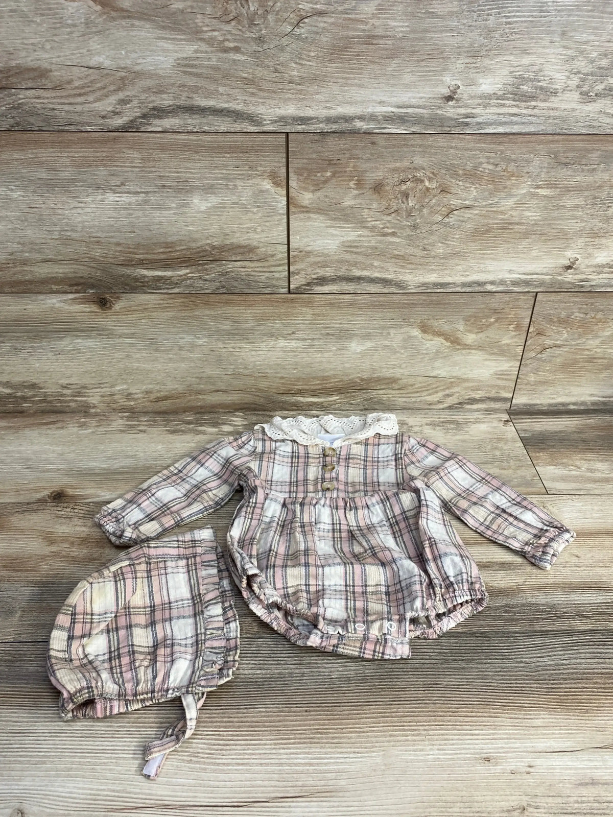 Pink and white plaid baby romper with lace collar and matching bonnet on wooden floor