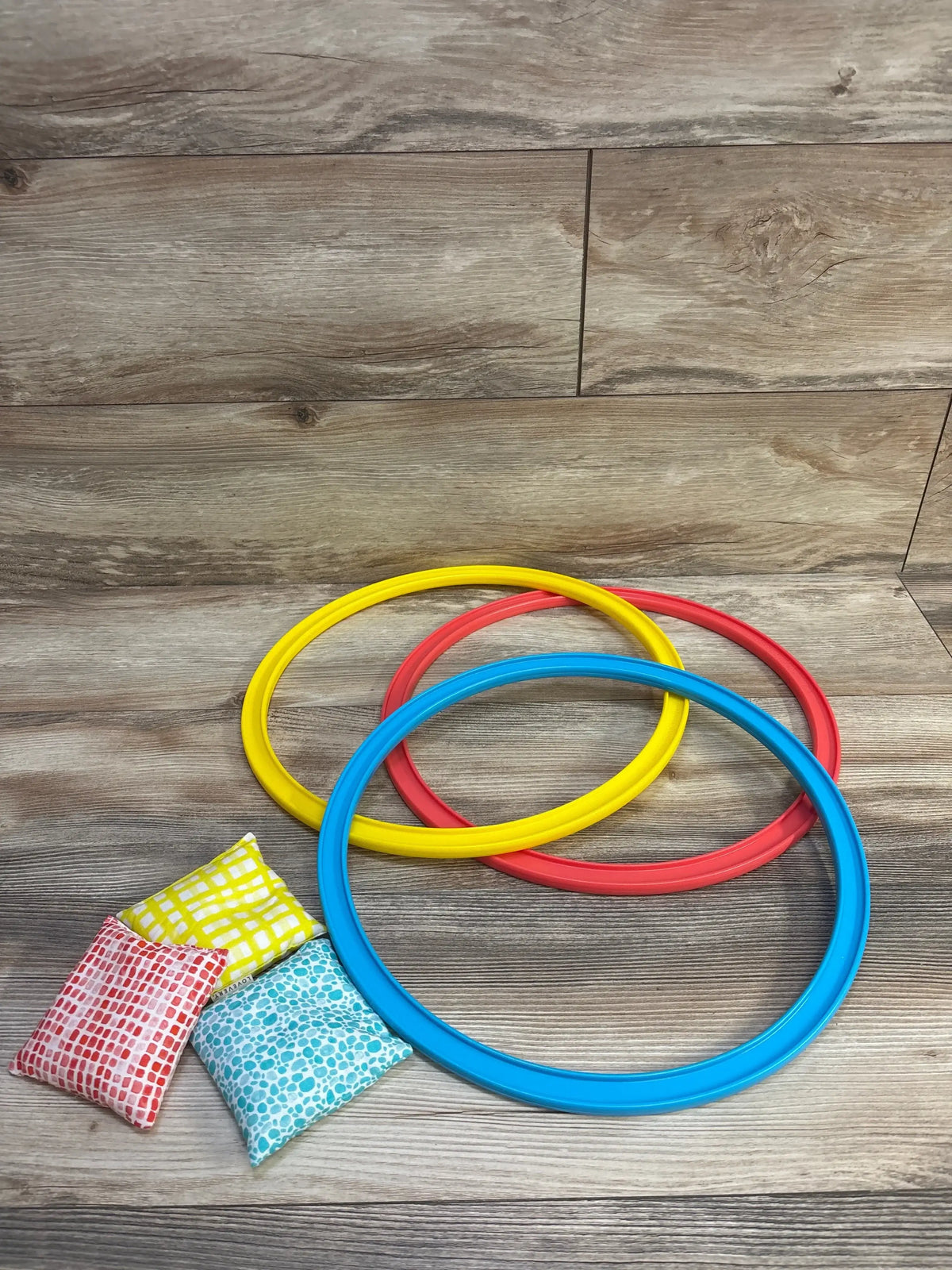 Overhead of Lovevery Jump-In Hoops and Bean Bags: 3 hoops (blue, yellow, red) and 3 patterned bean bags on wood floor