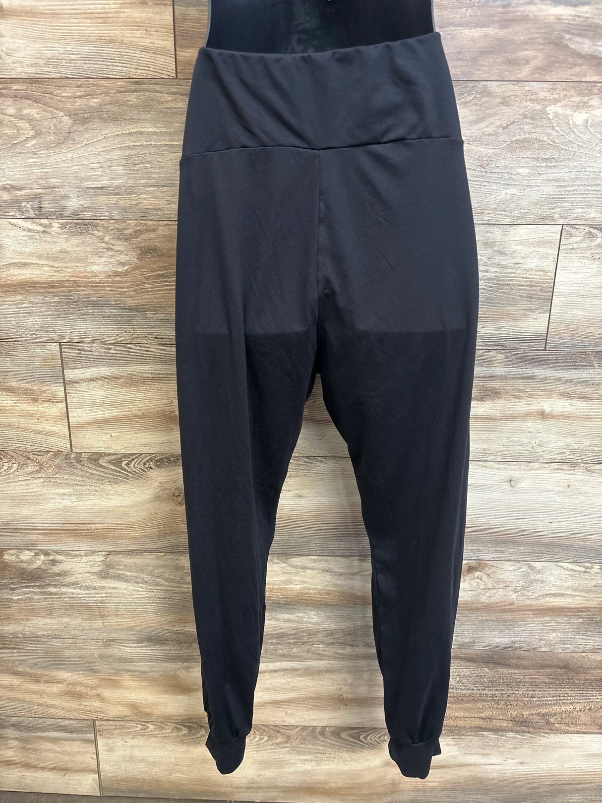 Front view of black maternity leggings (size Large) showcasing high fold-over waistband and cuffed ankles on a wood plank background