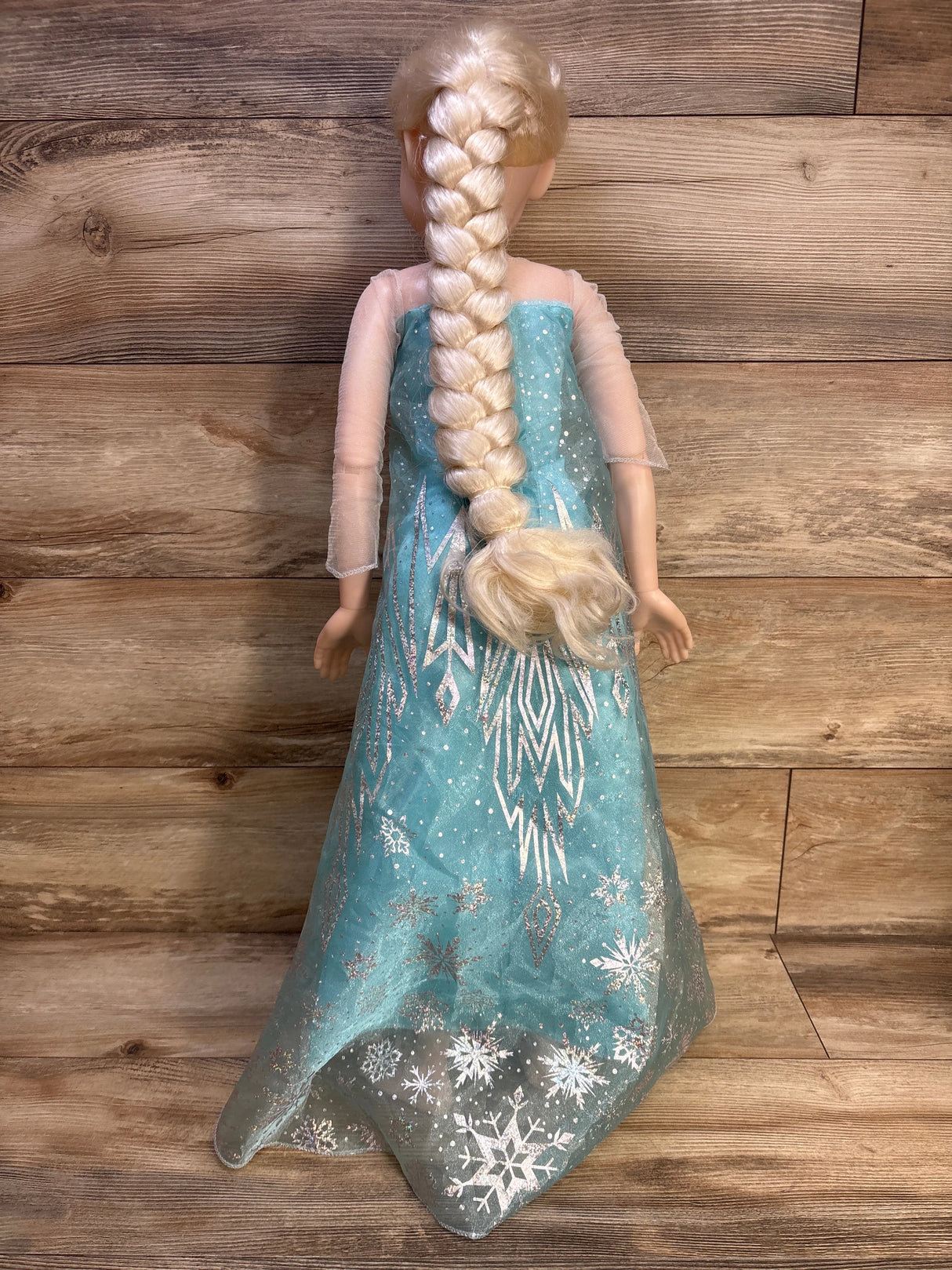 Rear view of 32-inch Jakks Elsa doll showing long braided blonde hair and turquoise snowflake dress on wood background