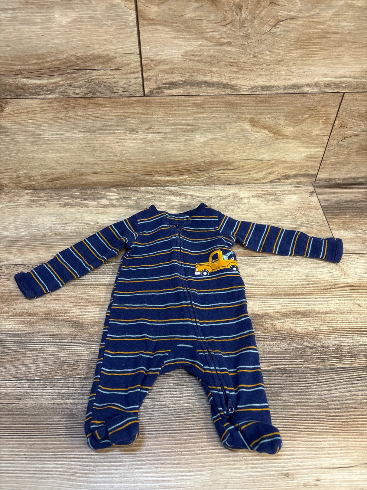 Navy blue striped baby sleeper with yellow truck patch, long sleeves, laid on wood floor