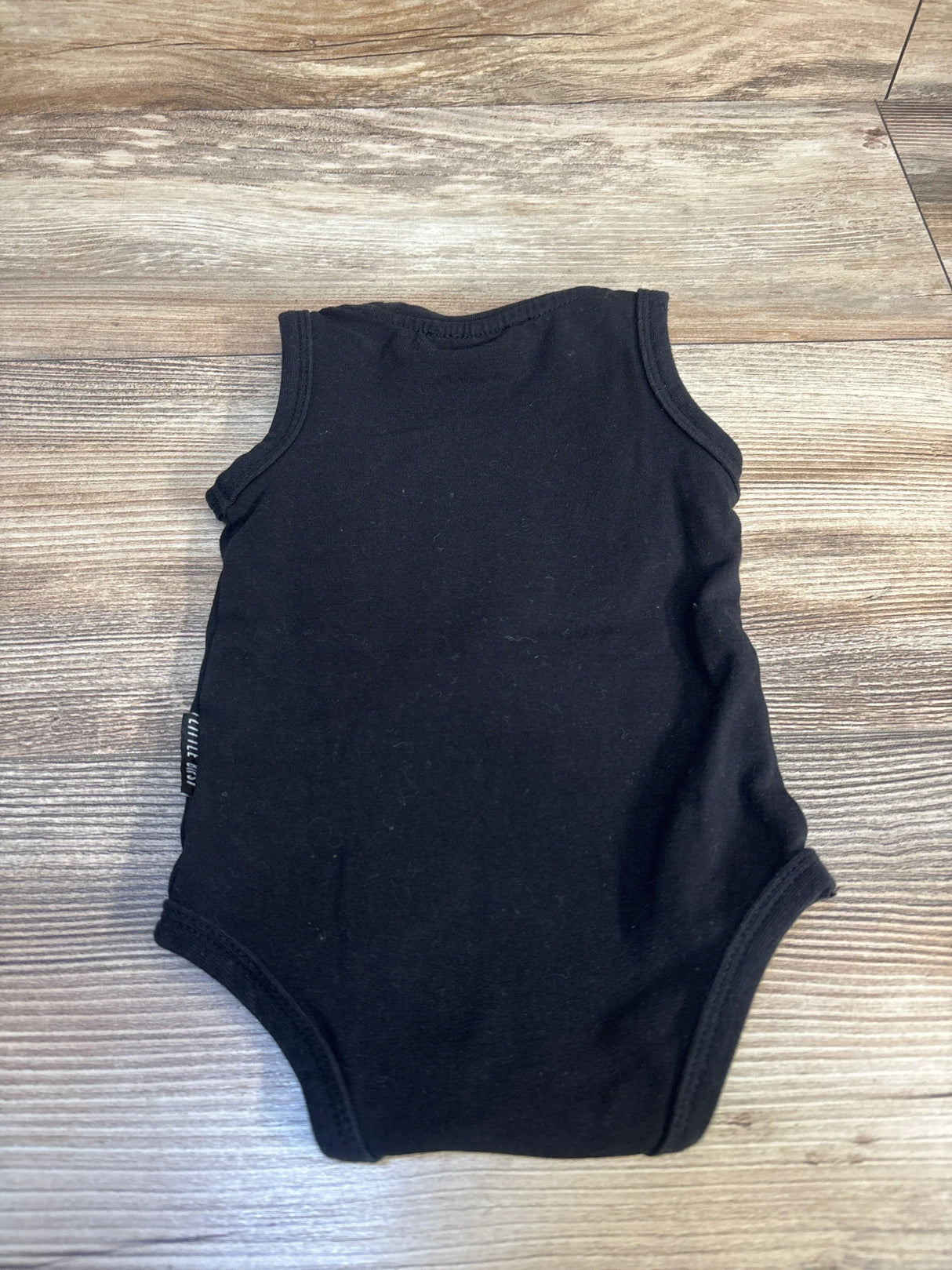 Black sleeveless baby bodysuit on wood floor, kids clothing resale product