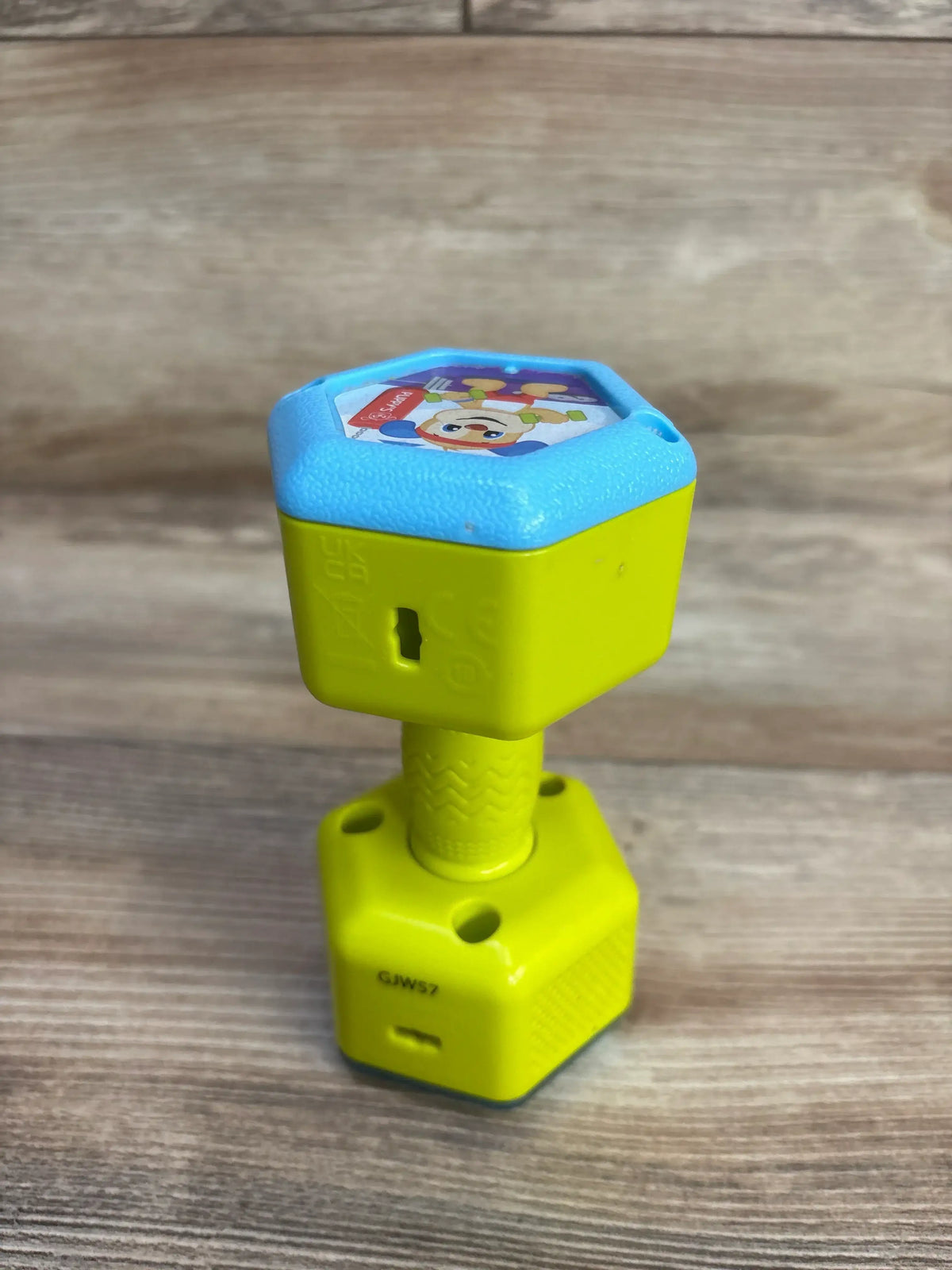 Angled view of Fisher-Price Countin' Reps dumbbell rattle showing textured grip and character sticker on wood background