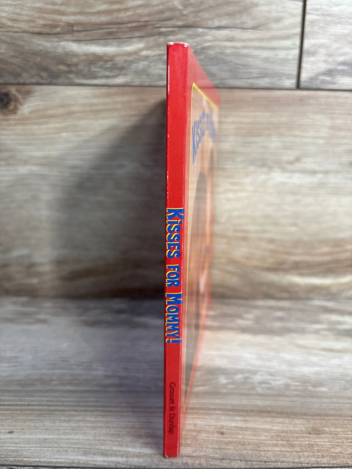 Spine of the red children's book titled Kisses for Mommy by Grosset & Dunlap on wooden surface
