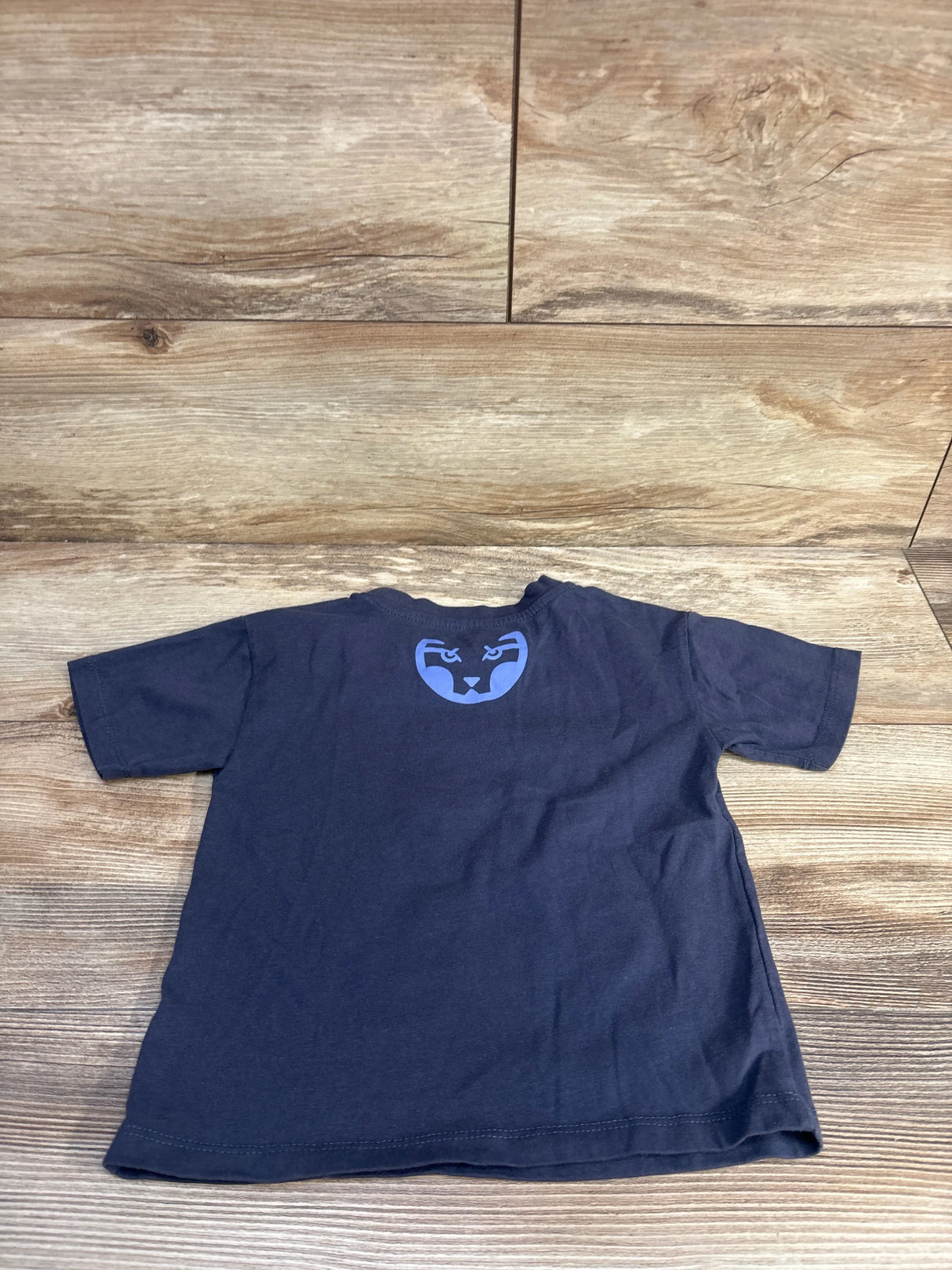 Back view of navy Marvel Black Panther toddler T-shirt, size 3T, showing blue panther face emblem at upper back on wood background
