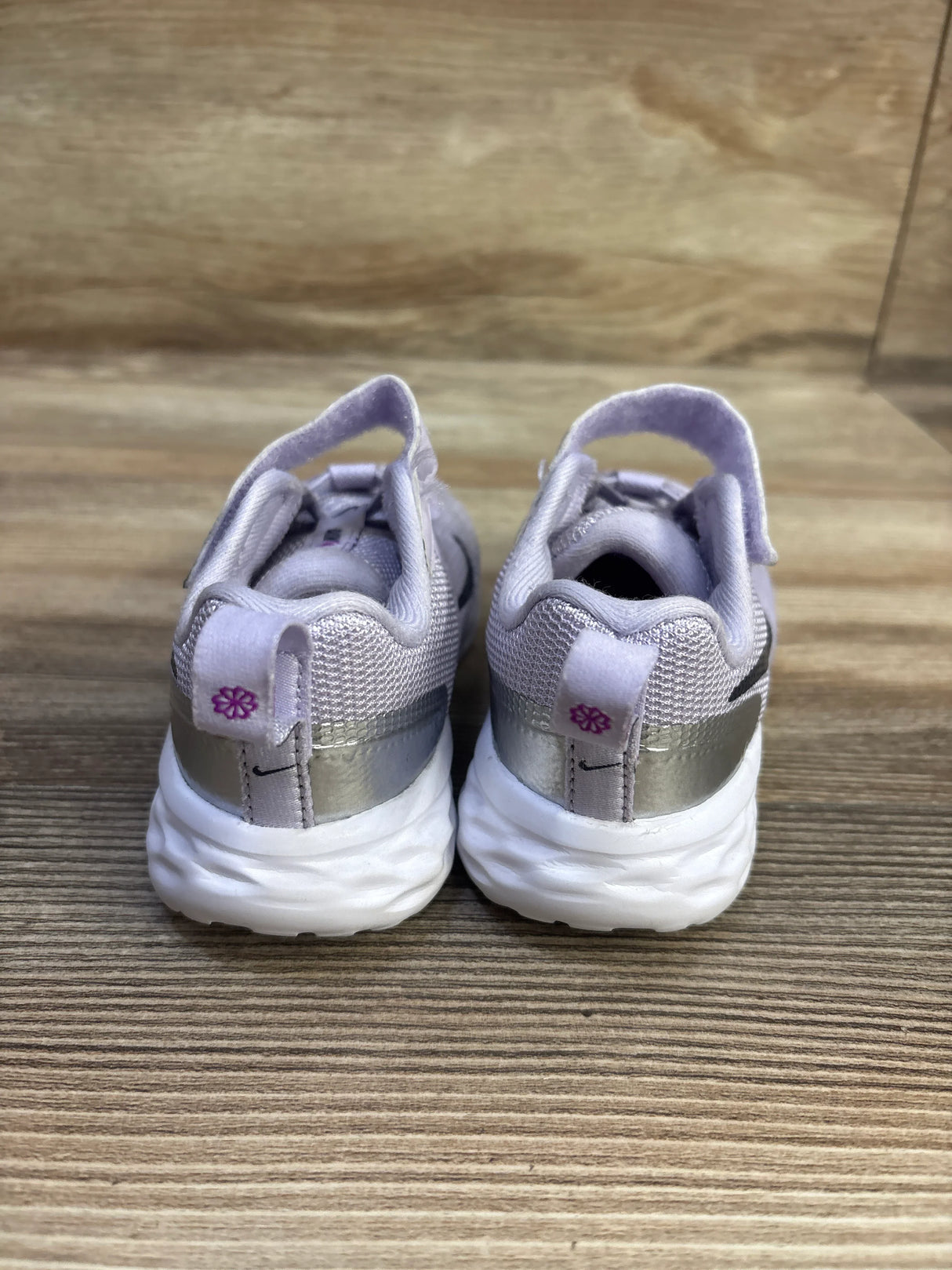 Rear view of Nike Revolution 6 TD sneakers in Violet Frost with silver heel band, lavender pull tabs, and white soles on wood