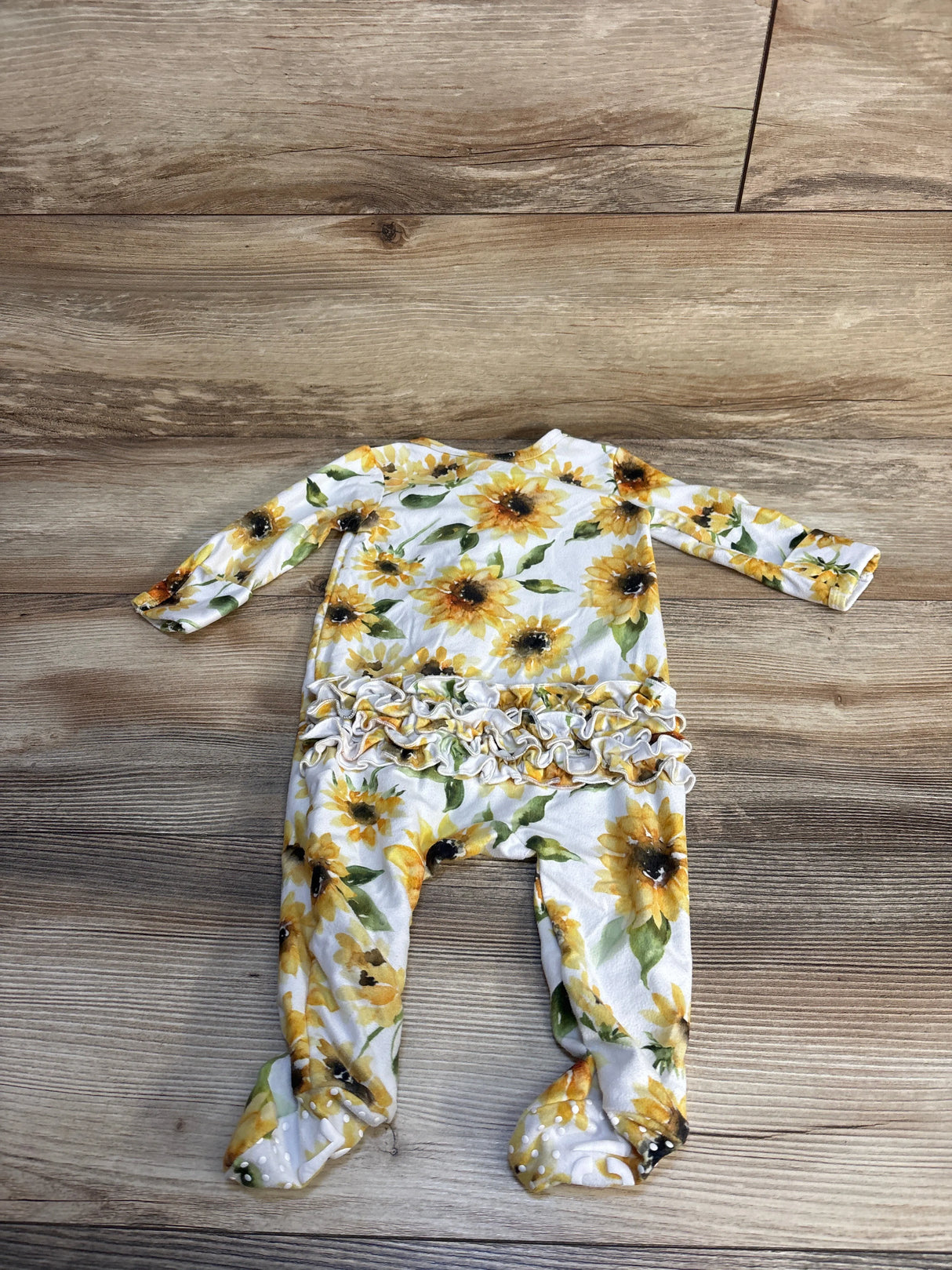 Flat lay of Caden Lane sunflower zipper ruffle footie size 3-6m showcasing yellow sunflower print on white with wood plank floor