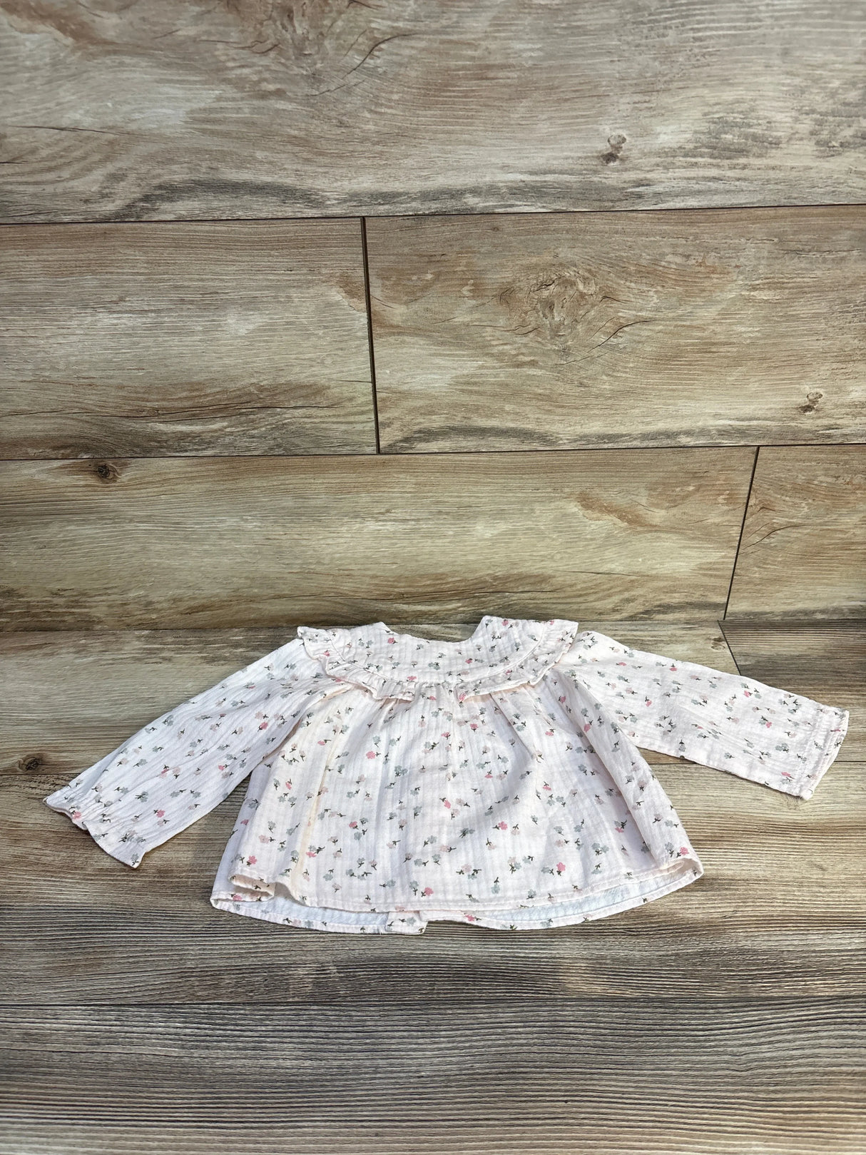 Floral baby blouse with ruffled collar on wooden floor