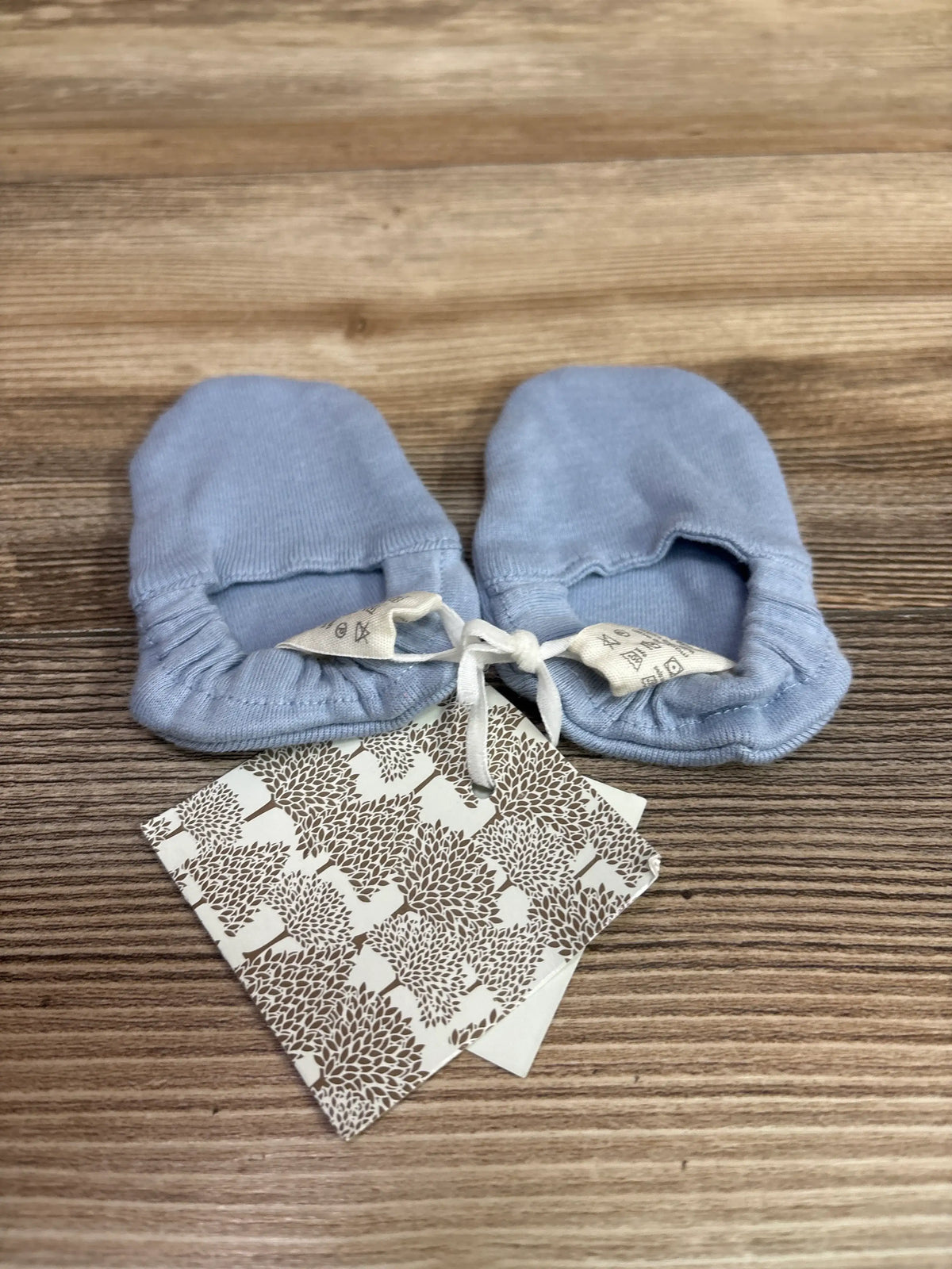 New Me n Mommy To Be blue baby booties with white ties on a wooden surface.