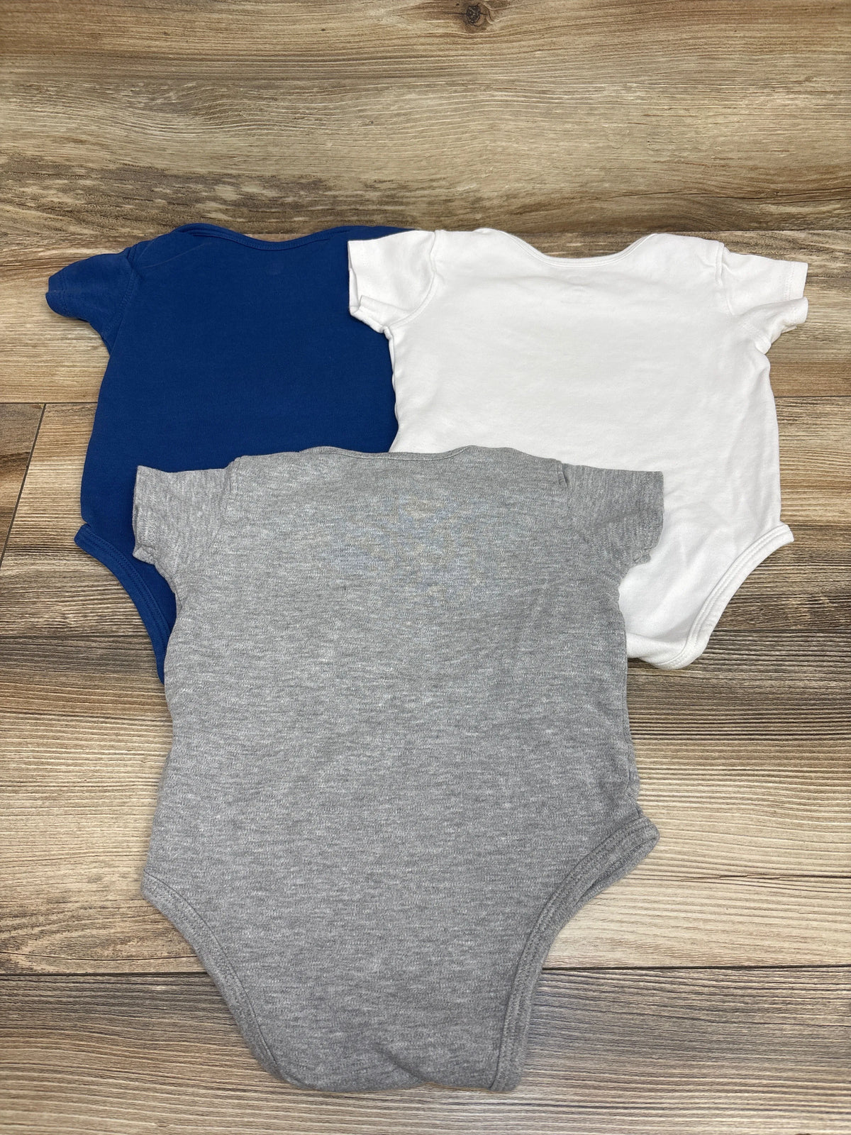 Top view of three NFL Indianapolis Colts baby bodysuits in navy, white, and gray on a wood surface
