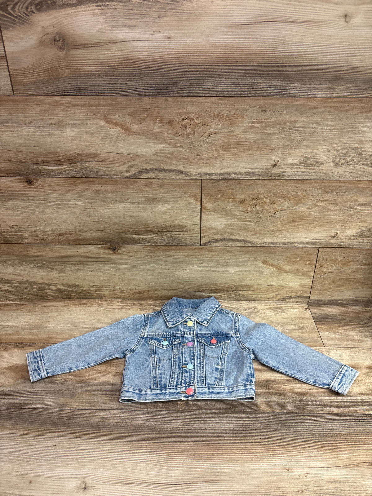 Old Navy blue denim jacket for toddlers size 2T with colorful buttons on a wood background