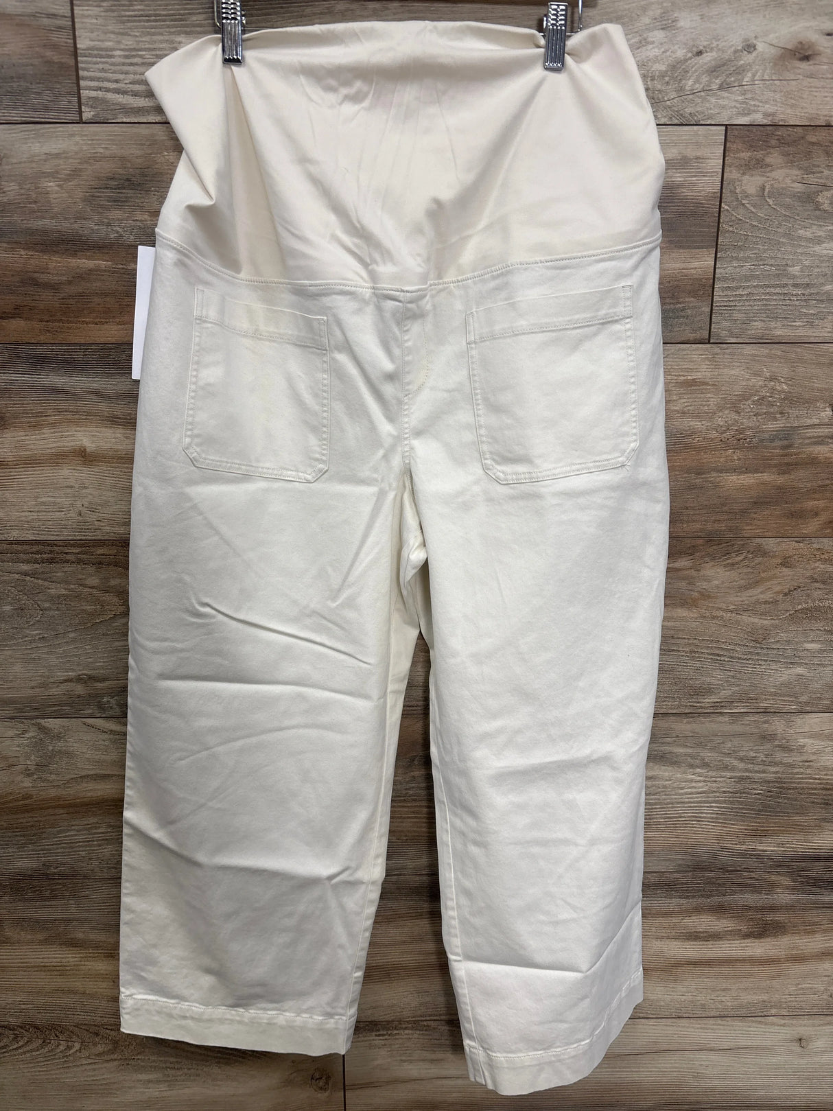 White maternity pants with elastic waistband and back pockets, displayed on wood background.
