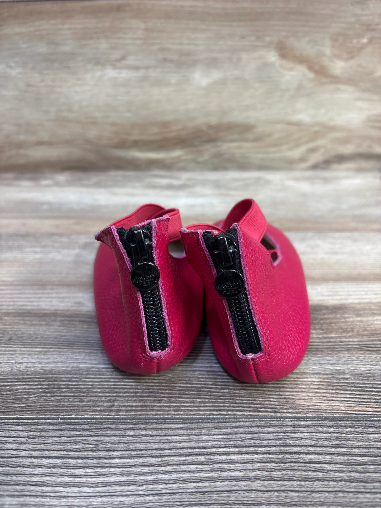 Rear view of pink Monkey Feet Mary Jane baby flats showing rear zipper pulls and criss-cross elastic strap on wood surface