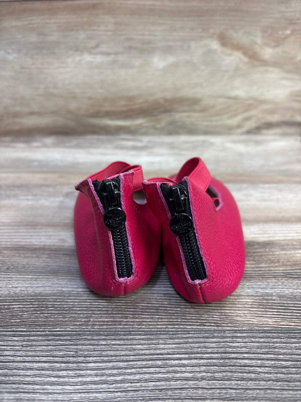 Rear view of pink Monkey Feet Mary Jane baby flats showing rear zipper pulls and criss-cross elastic strap on wood surface