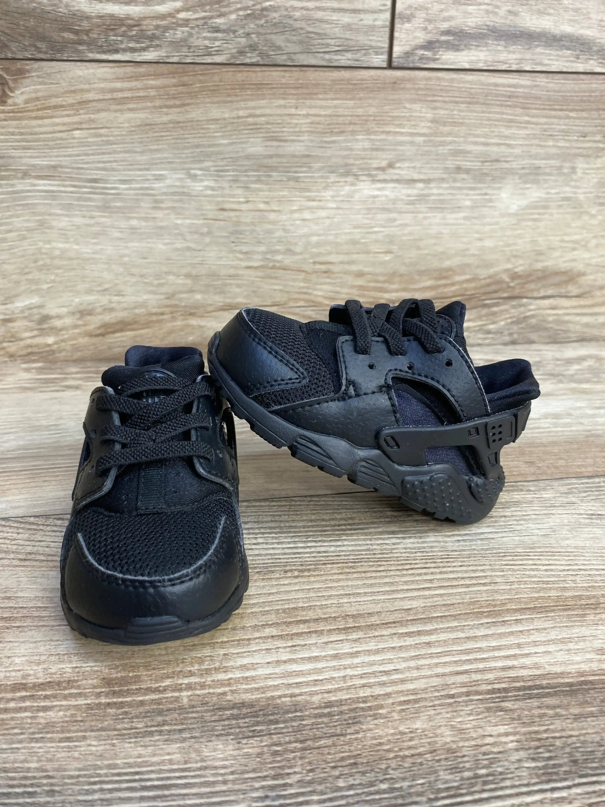 Side and front view of Nike Air Huarache Run triple black sneakers size 5C showing mesh and leather upper on wood floor