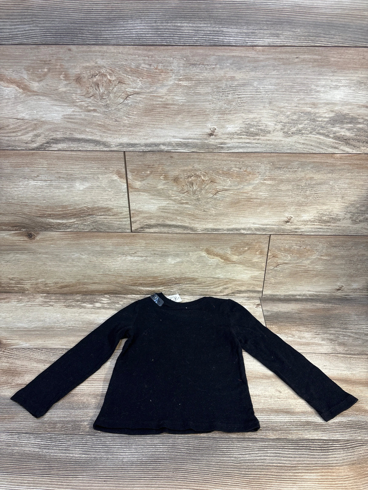 Flat lay of Children's Place black long-sleeve toddler shirt, size 2T, new with tags on wood background