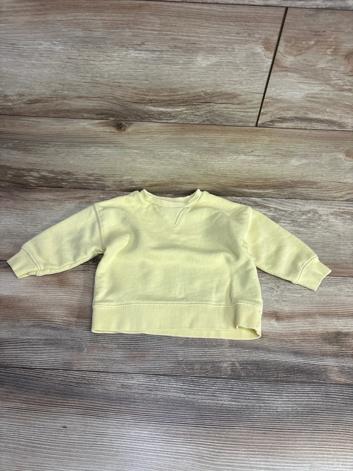 Front flat lay of Zara yellow baby sweatshirt size 6-9 months showcasing crewneck and ribbed cuffs and hem on wood background