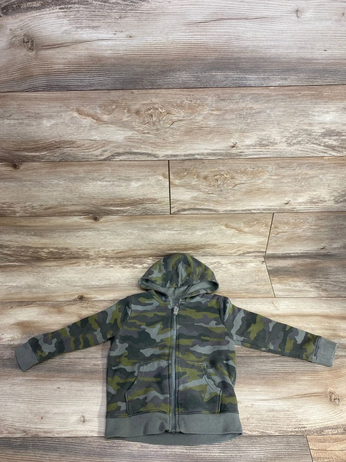 Children's camouflage zip-up hoodie with hood and front pockets on wooden floor background