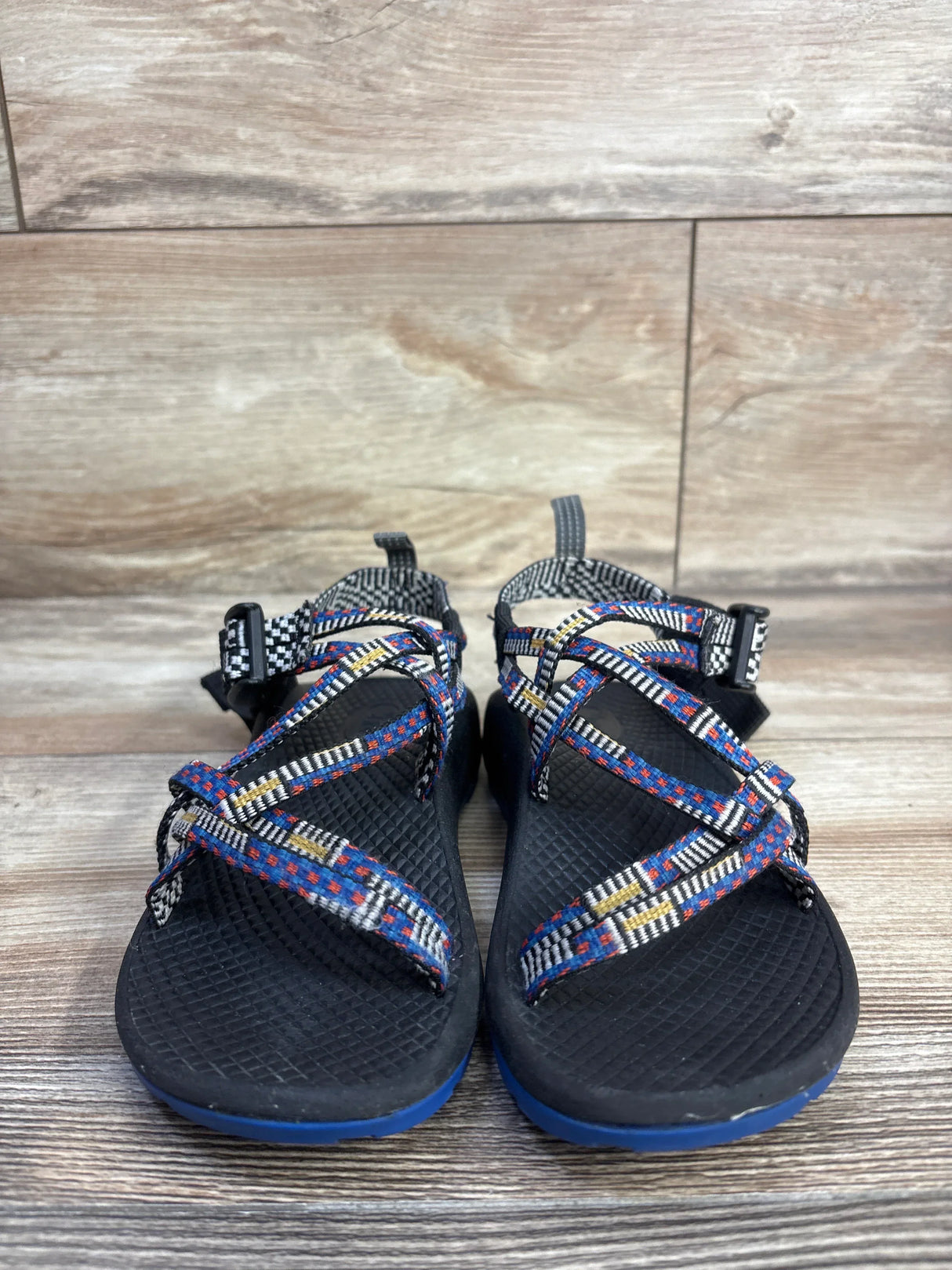 Front view of Chaco ZX/1 Ecotread sandal showing black footbed, multicolor woven straps and blue sole on wood floor