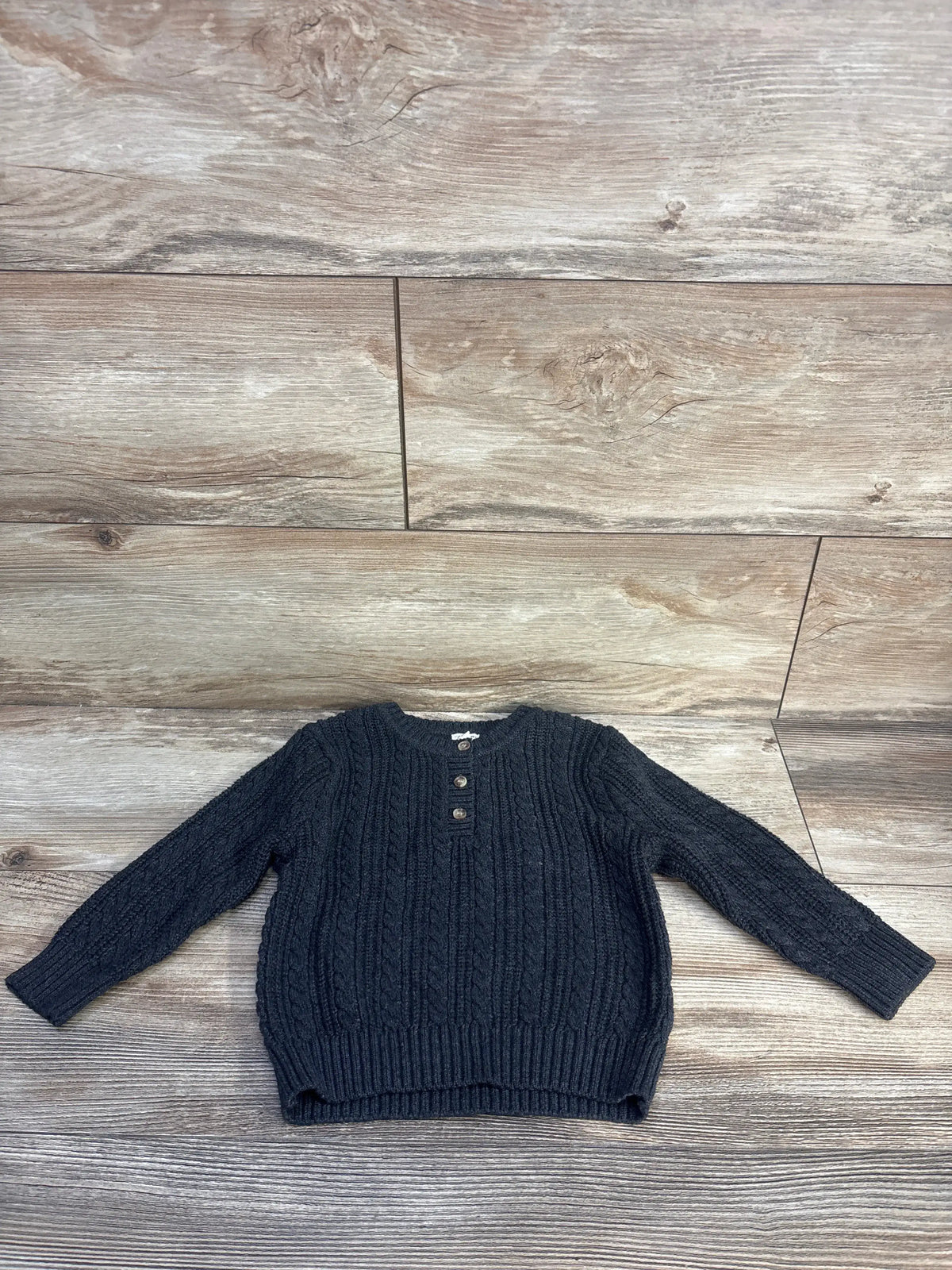 Front view of Tahari cable knit henley sweater in grey showcasing textured cable knit pattern and henley neckline on a wood surface