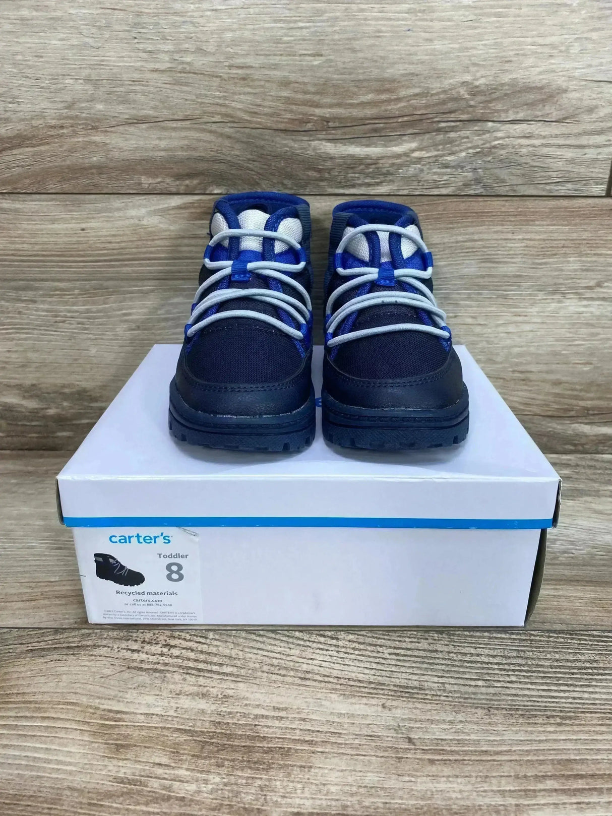 Front view of Carter’s toddler Fallon boots, navy with white laces, on box with visible size 8 label on wood floor