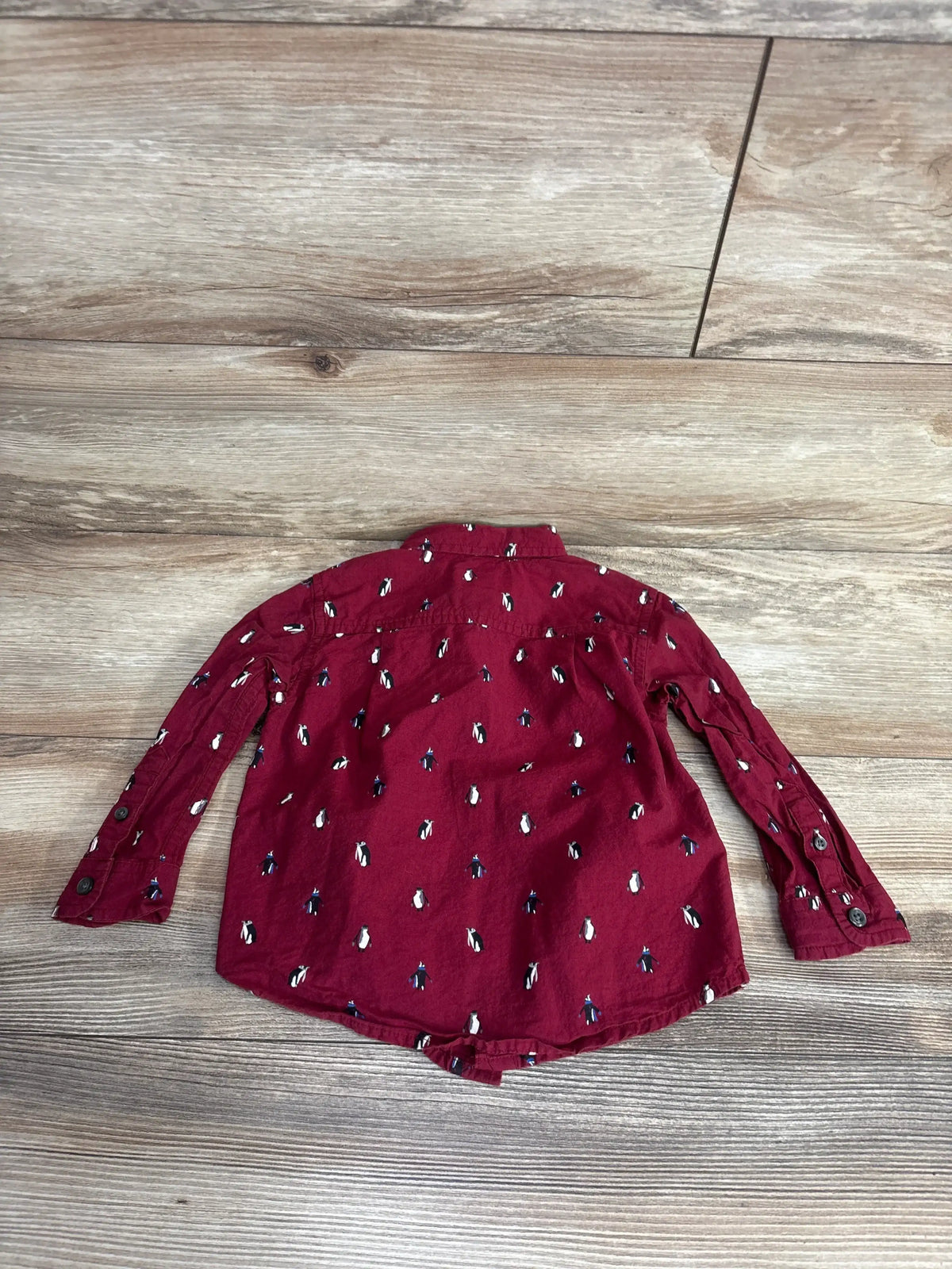Maroon long sleeve toddler shirt with penguin print, laid flat on wooden floor