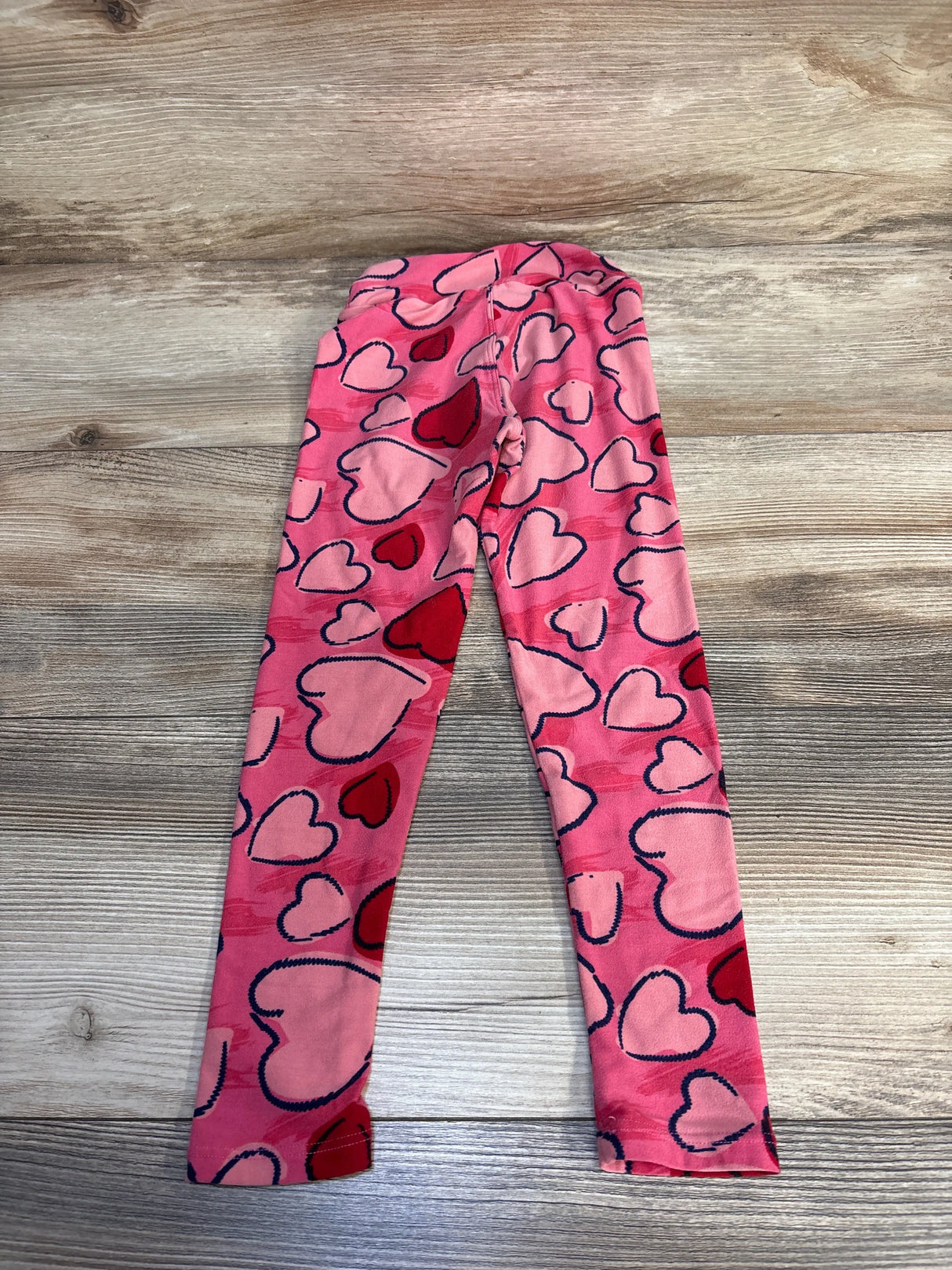 Pink kids leggings with red and pink heart pattern on wooden background