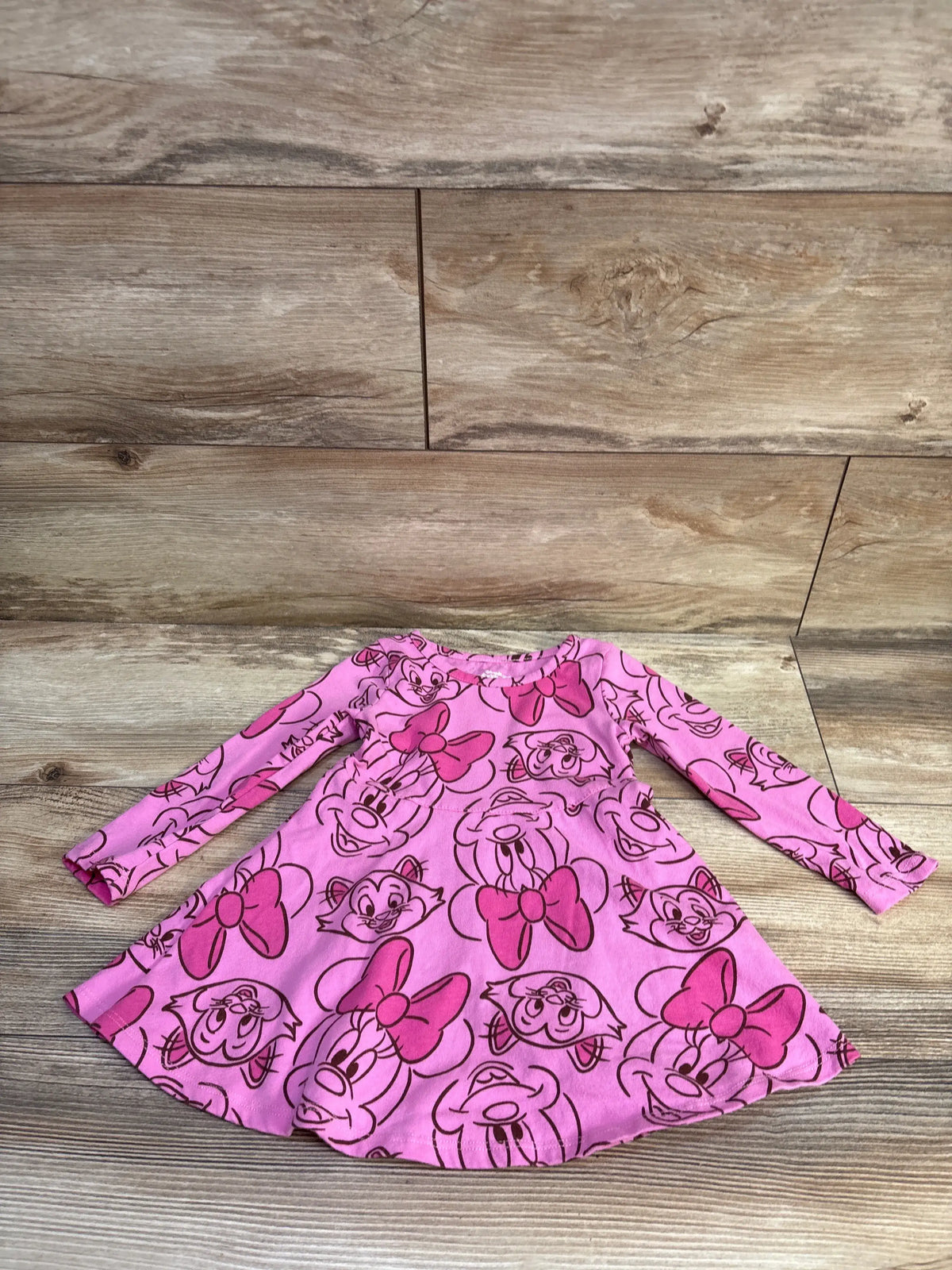 Flat lay of Disney Minnie Mouse long sleeve dress with all over Minnie face print and flared skirt on wood floor