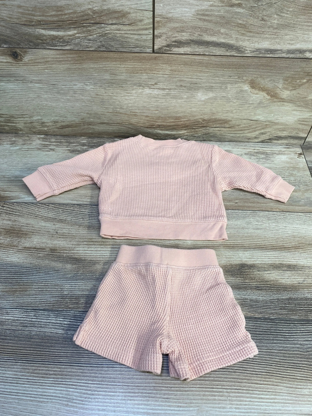 Flat lay of Carter's x Hilary Duff newborn pink thermal two-piece set showing waffle knit texture on a wood floor background
